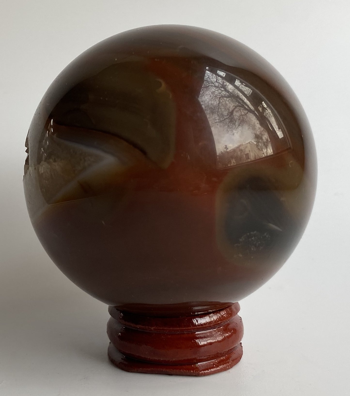 Sfera din cristal de agat rosu, pe suport din lemn, cu fundal alb sub lumina naturala