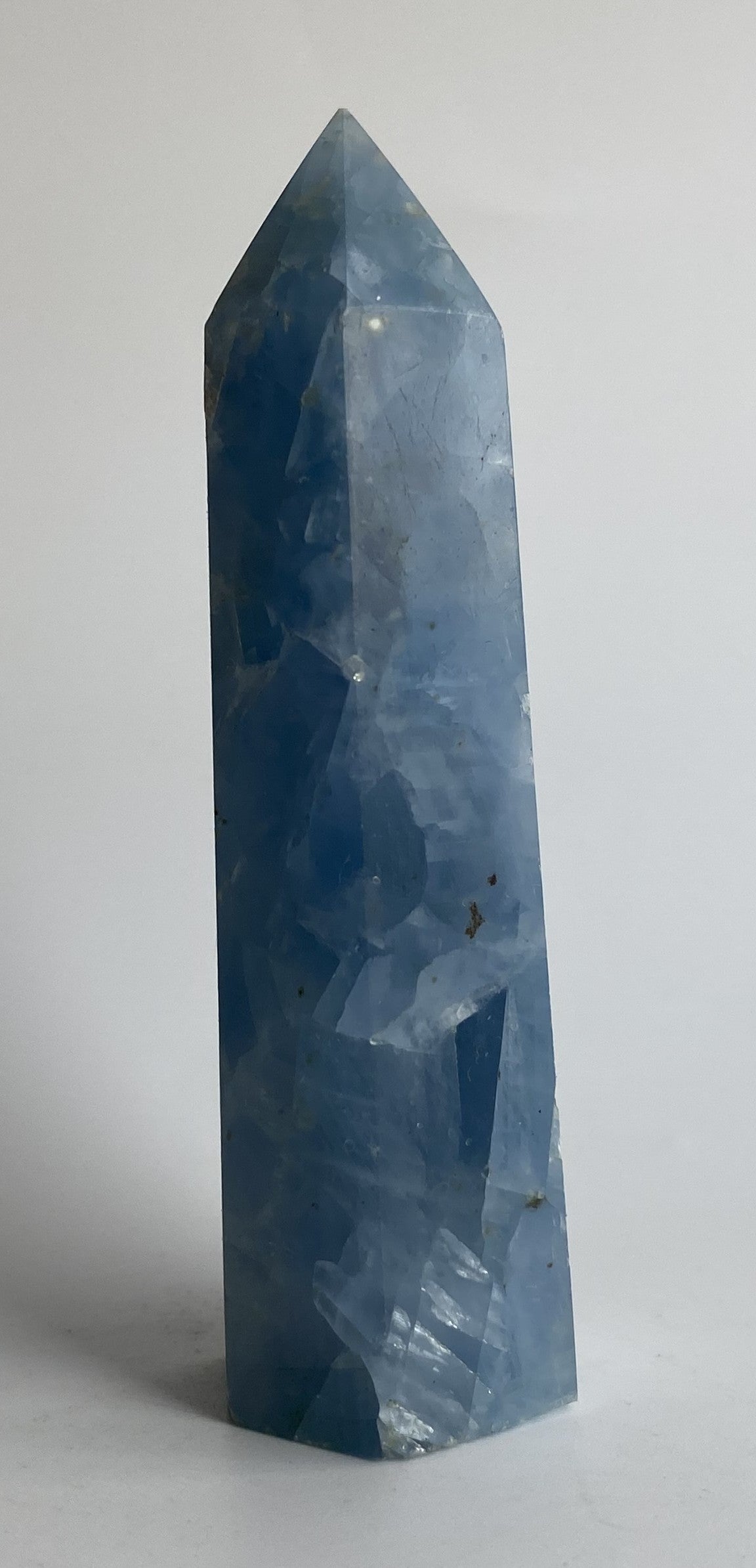 Obelisc din cristal de calcit albastru pe fundal alb sub lumina naturala