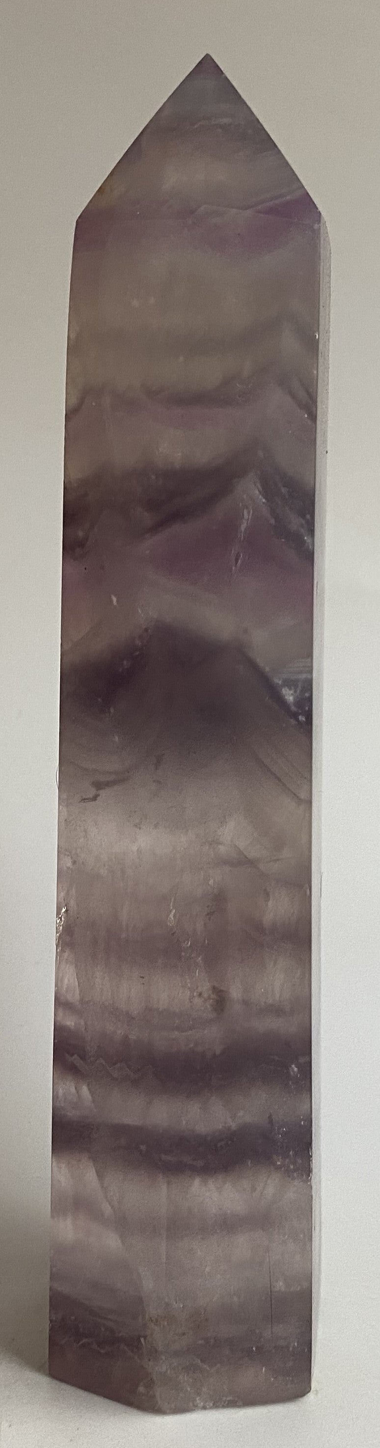 Obelisc din cristal de fluorit mov pe fundal alb sub lumina naturala
