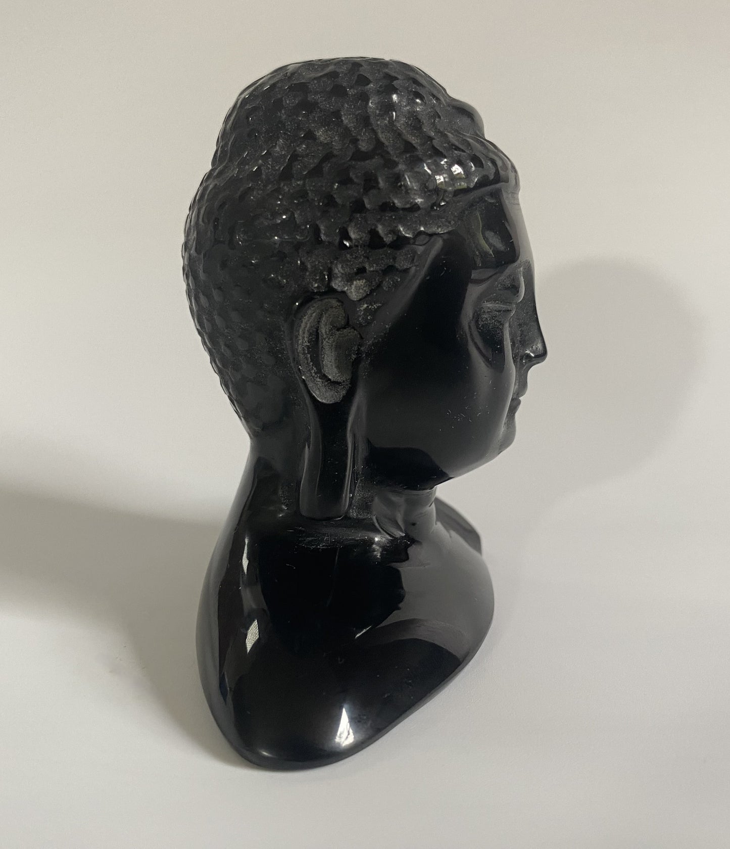 Sculptura cap de Buddha din obsidian negru cu fundal alb sub lumina naturala