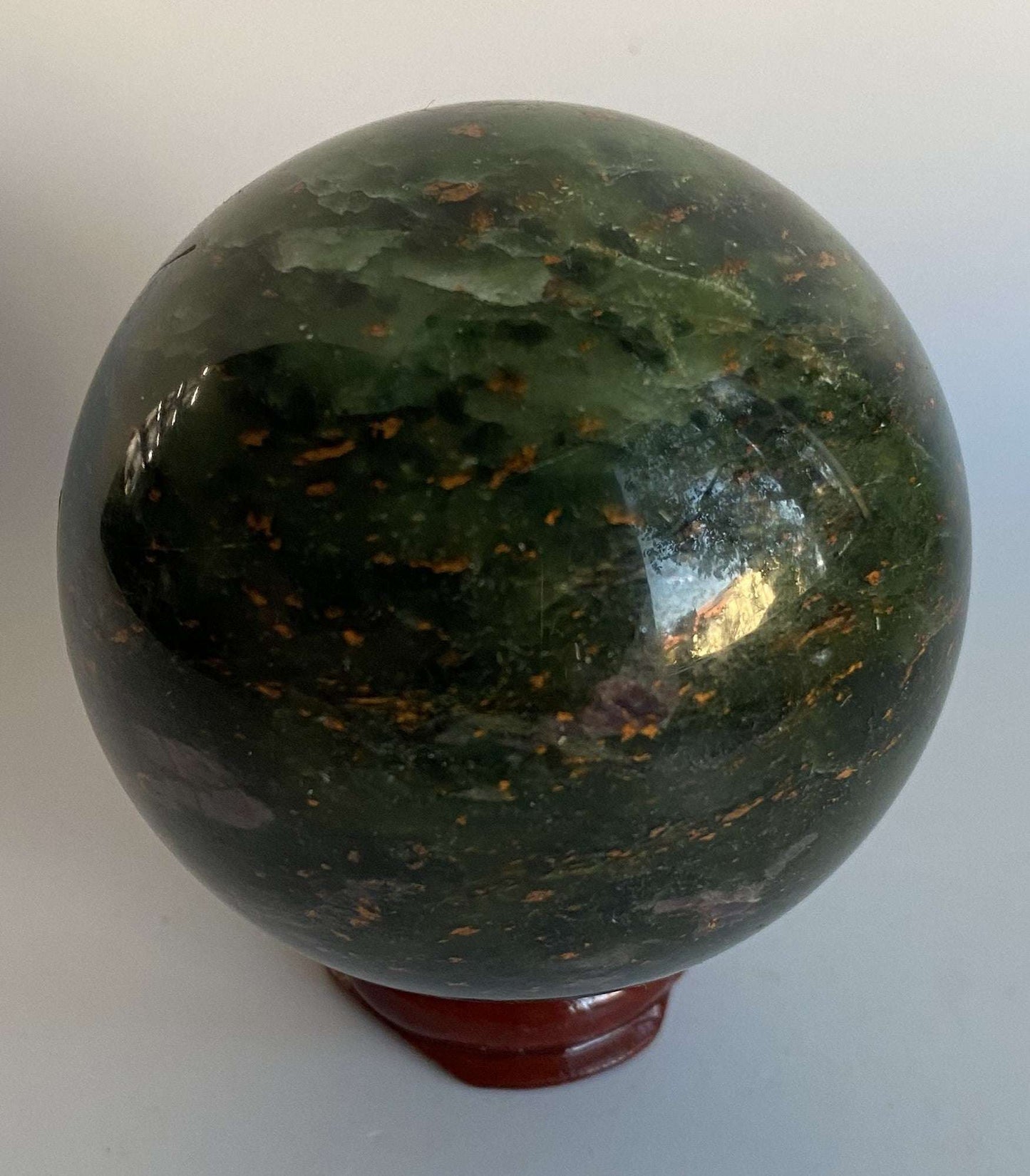 Polished green Corindon in Zoisit sphere with pink-violet flower patterns on wooden stand