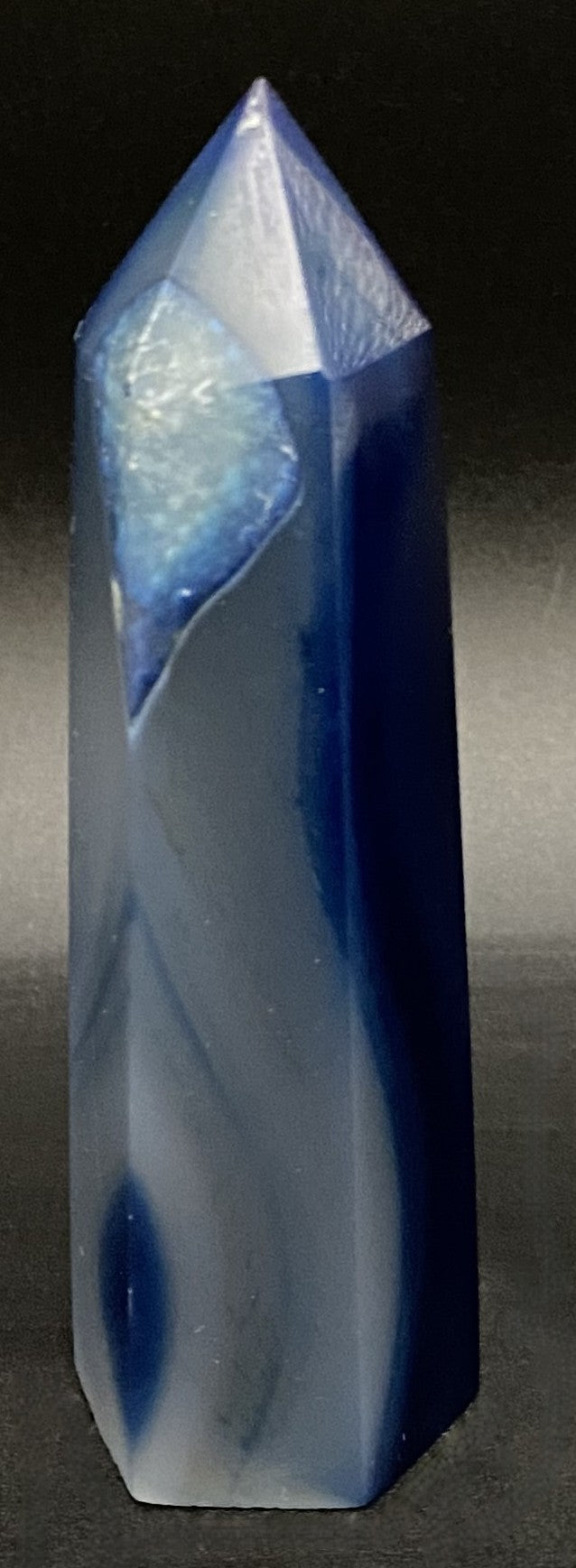 Obelisc din cristal de agat albastru pe fundal negru sub lumina artificiala