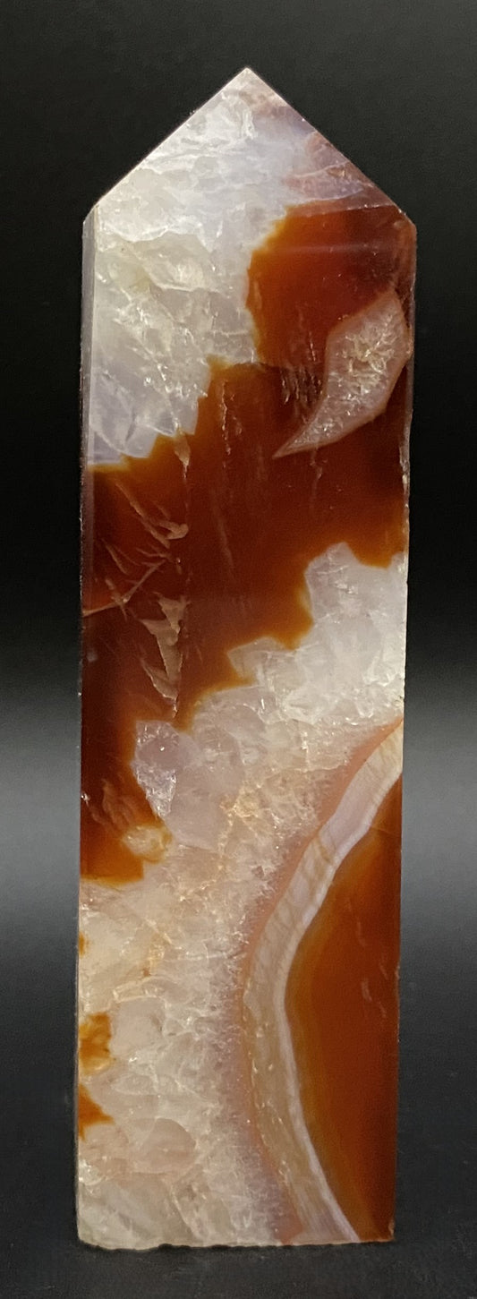 Obelisc din cristal de agat rosu pe fundal negru sub lumina artificiala