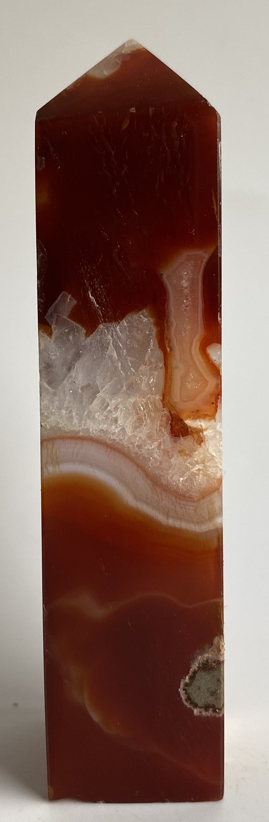 Obelisc din cristal de agat rosu pe fundal alb sub lumina naturala