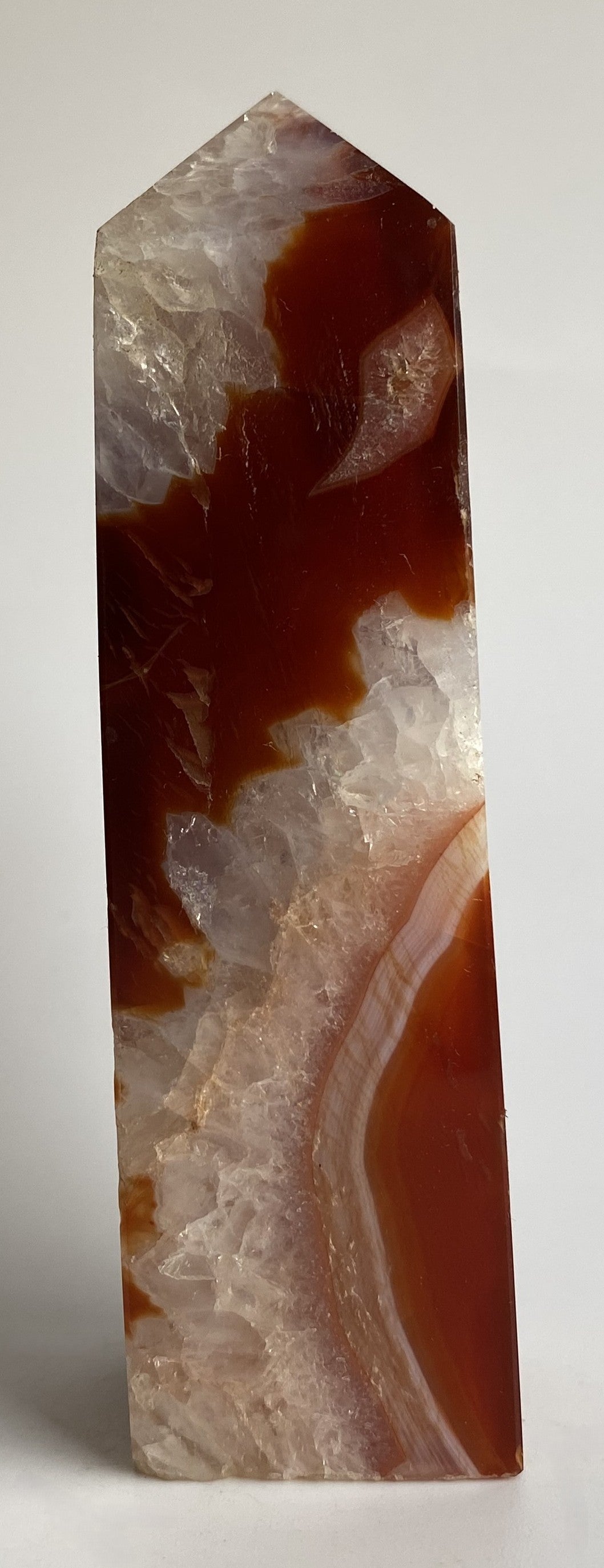 Obelisc din cristal de agat rosu pe fundal alb sub lumina naturala