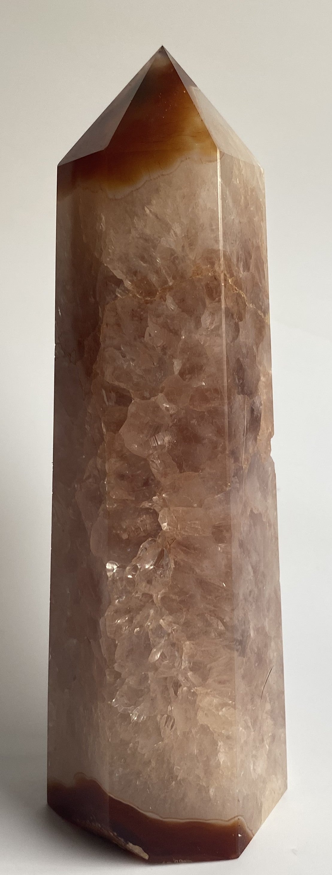 Obelisc din cristal de agat rosu pe fond alb sub lumina naturala