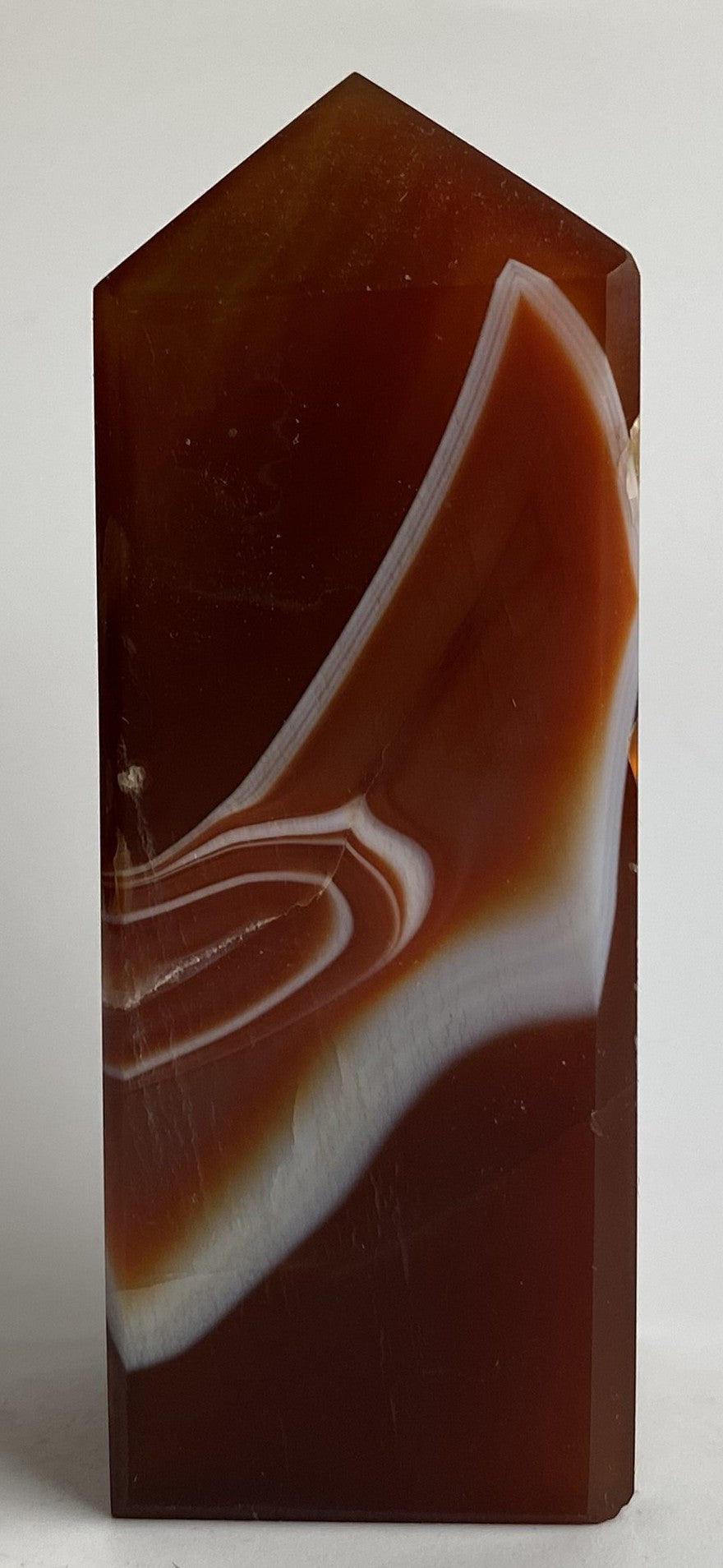 Obelisc din cristal de agat rosu pe fundal alb sub lumina naturala