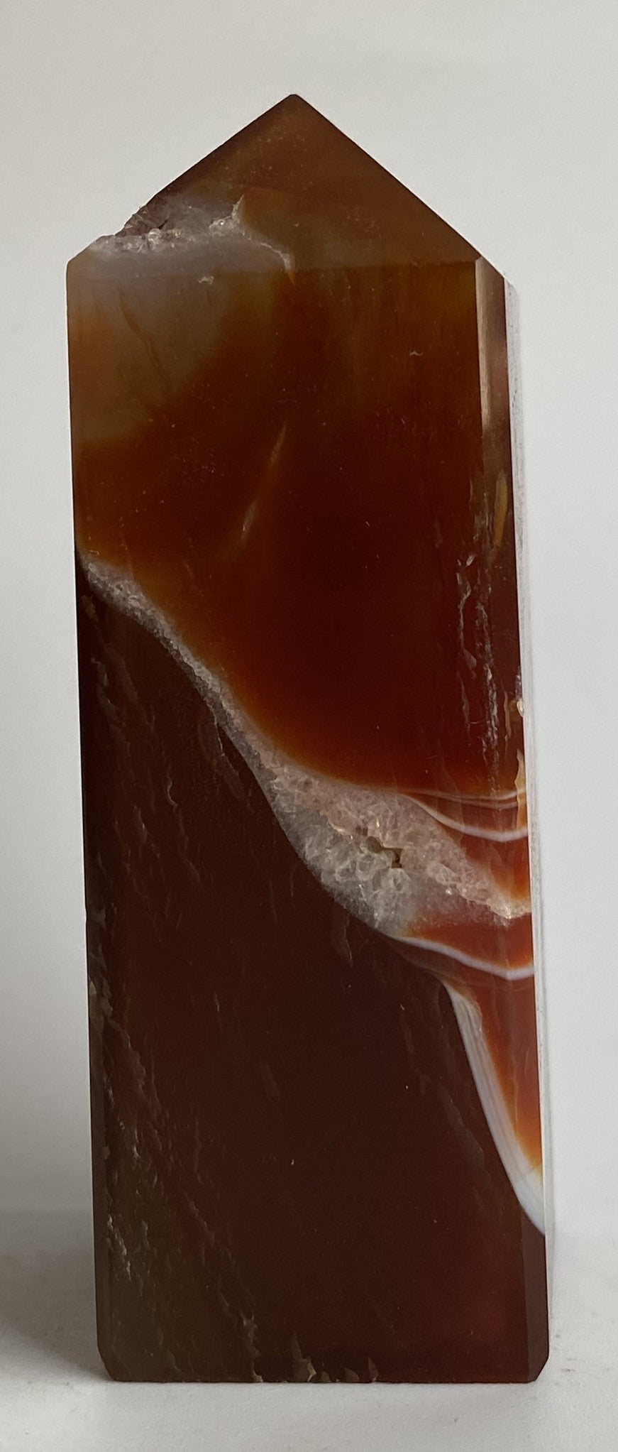 Obelisc din cristal de agat rosu pe fundal alb sub lumina naturala