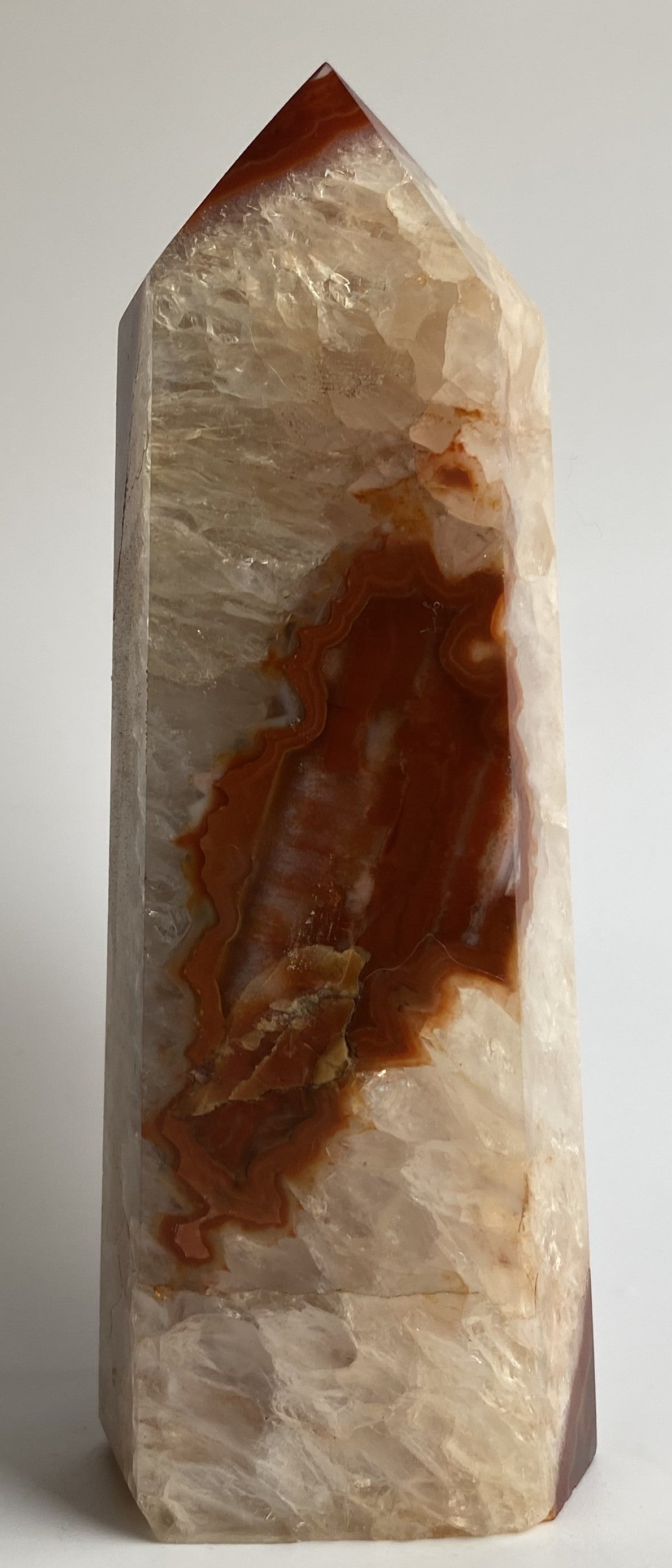 Obelisc din cristal de agat rosu pe fundal alb sub lumina naturala