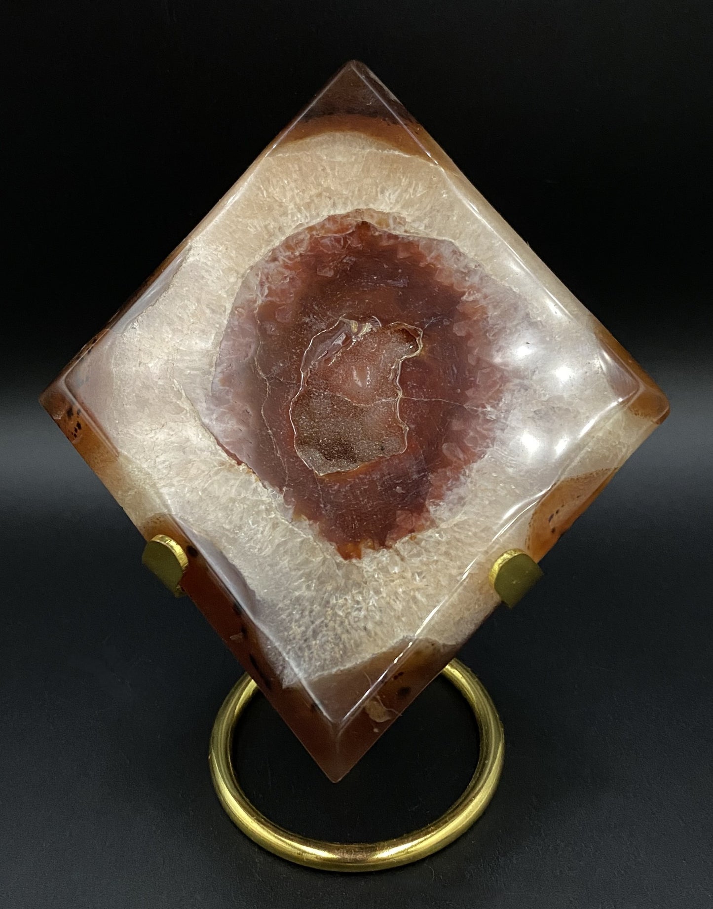 Romb din cristal de agat rosu pe suport metalic auriu, cu fundal negru sub lumina artificiala