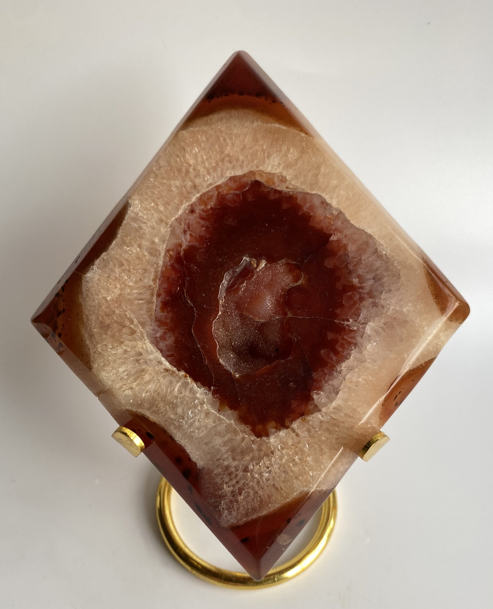 Romb din cristal de agat rosu pe suport metalic auriu, cu fundal alb sub lumina naturala
