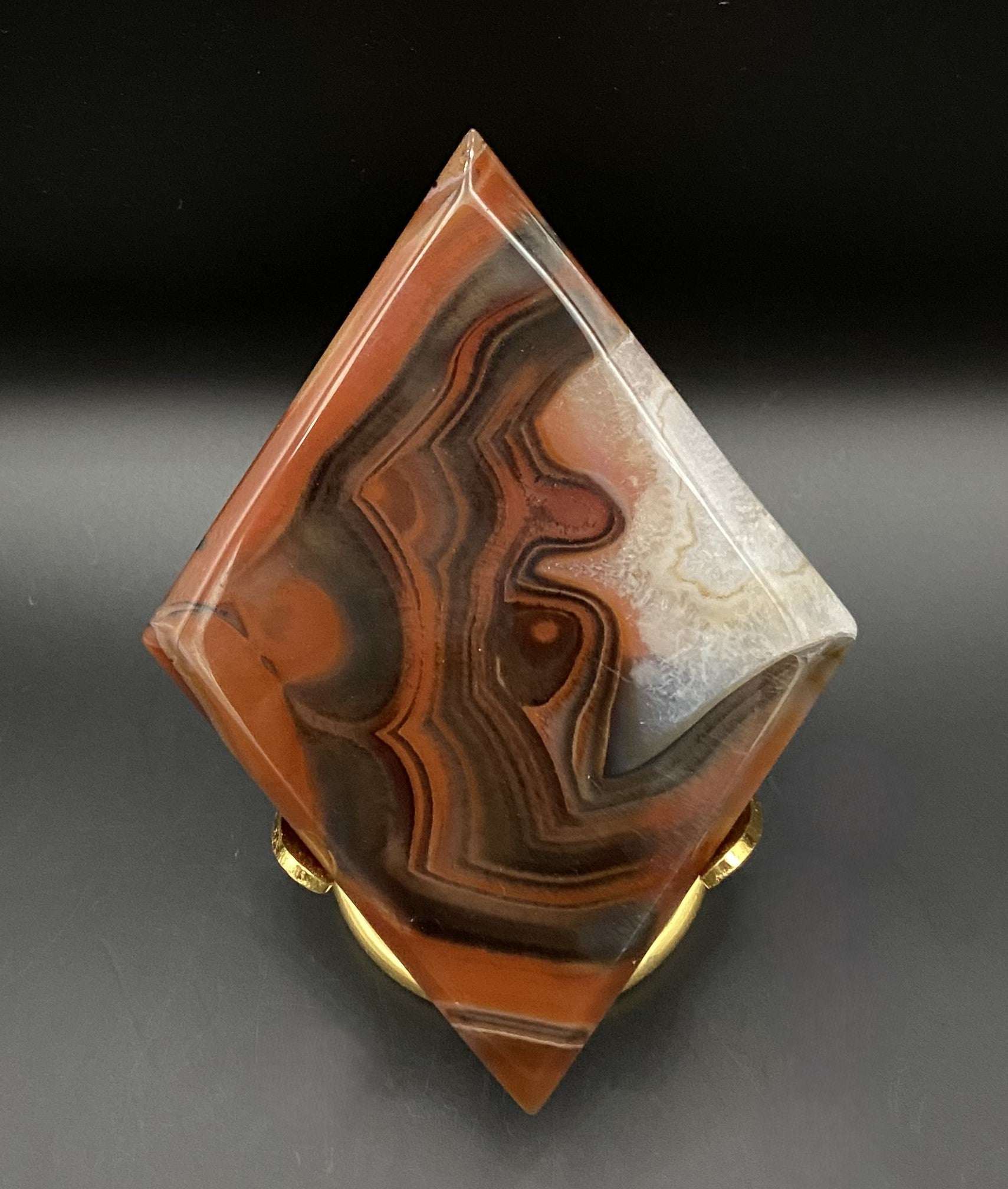 Rhomboid red agate stone with metal stand on black background