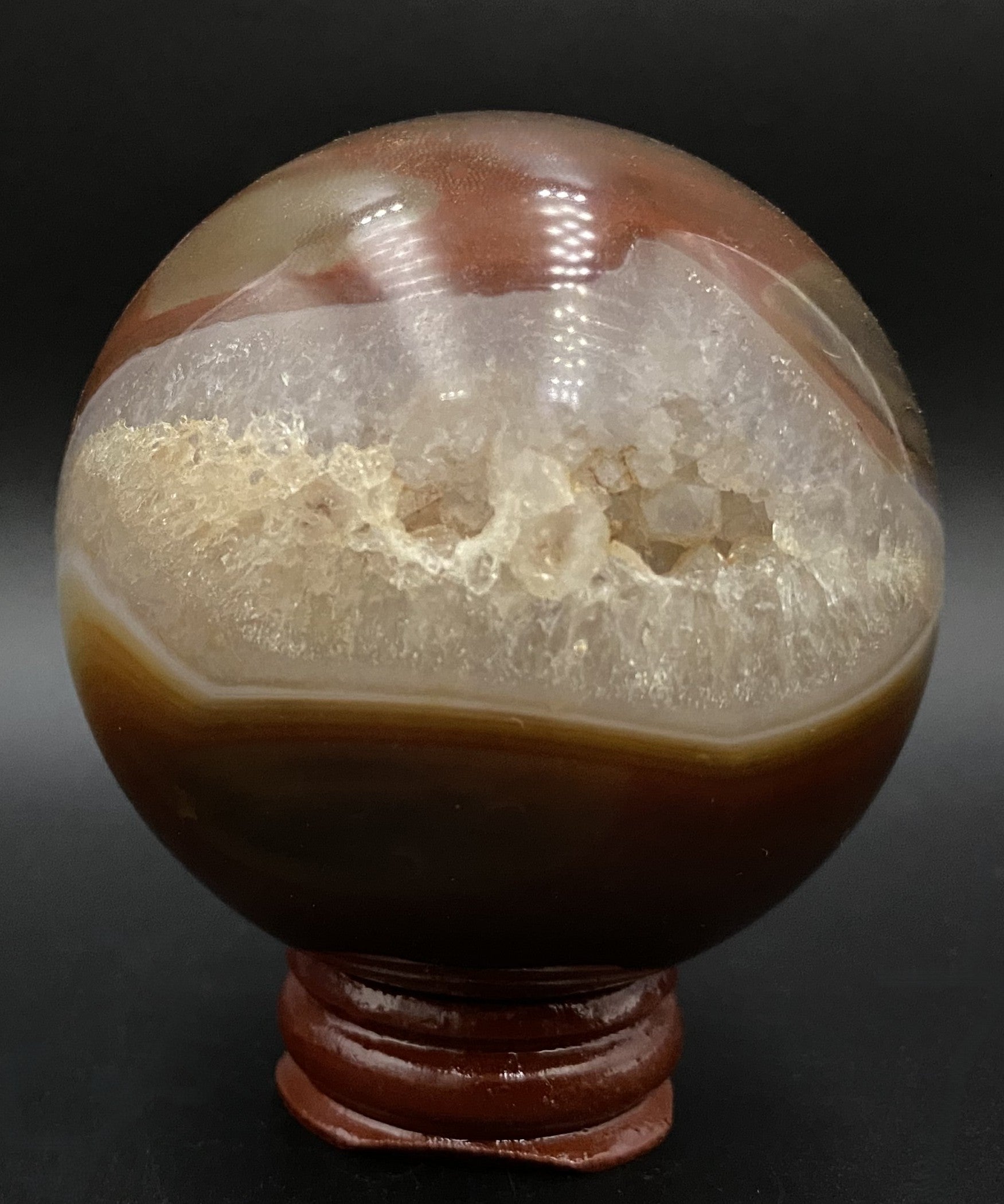 Sfera din cristal de agat rosu, pe suport din lemn, cu fundal negru sub lumina artificiala