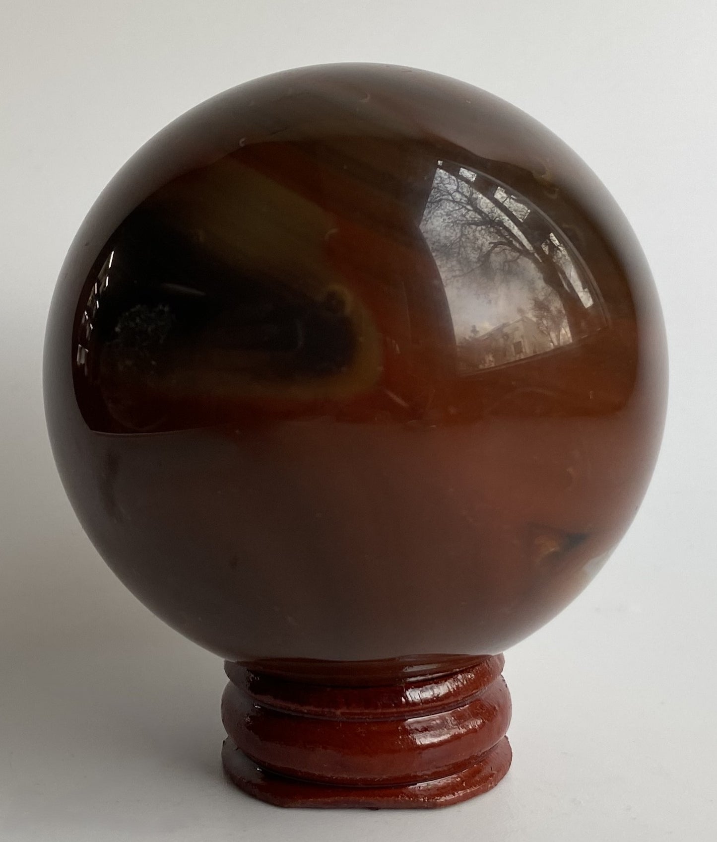Sfera din cristal de agat rosu, pe suport din lemn, cu fundal alb sub lumina naturala