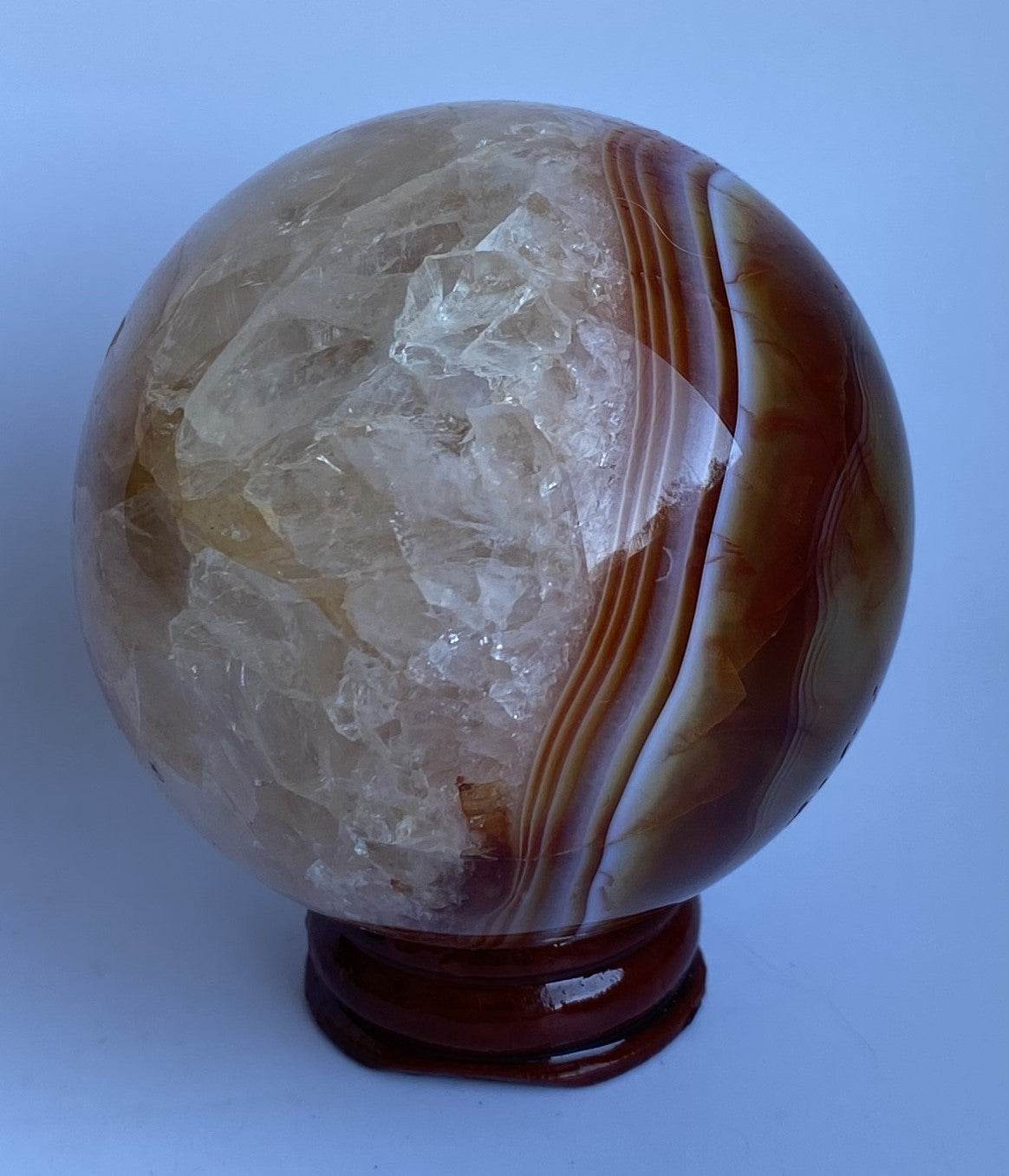 Sfera din Agat Rosu pe suport din lemn natural, piatra semipretioasa cu texturi cristaline si dungi distincte.