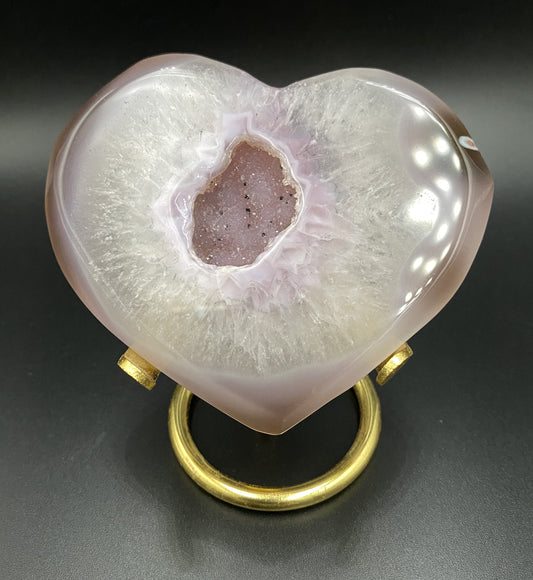 Inima din agat roz pe suport metalic auriu pe fond negru sub lumina artificiala