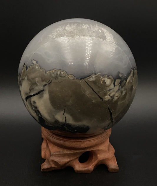 Sfera din cristal de agat vulcanic pe suport din lemn, pe fundal negru sub lumina artificiala