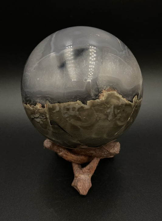 Sfera din cristal de agat vulcanic pe suport din lemn pe fundal negru, sub  lumina artificiala