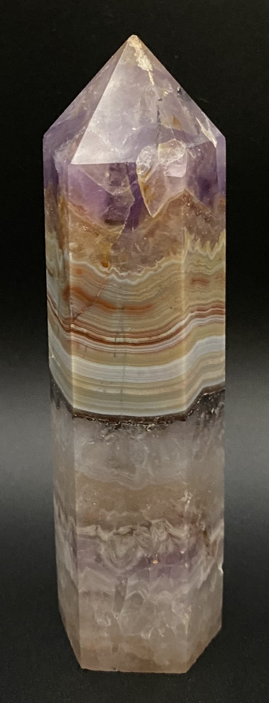 Obelisc din mineral simbiot de agat si ametist pe fundal negru sub lumina artificiala