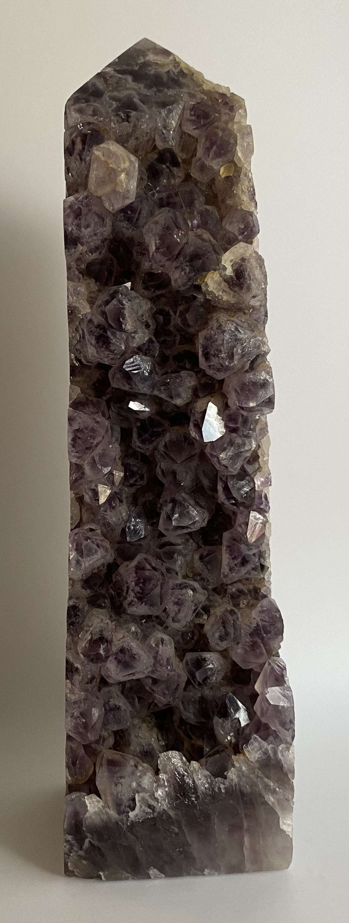Obelisc din geoda de ametist cu cristale violet închis pe fundal alb