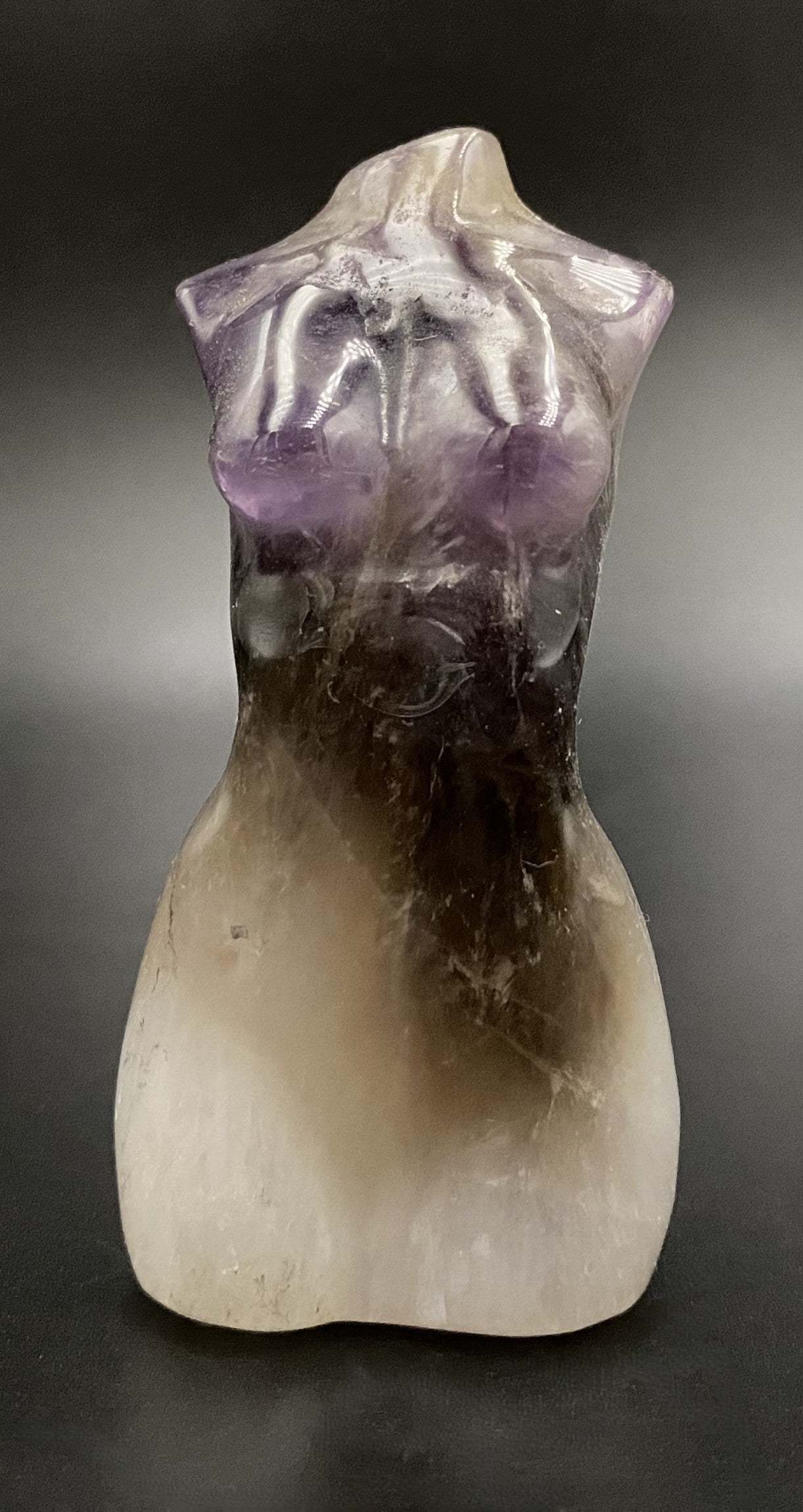 Sculptura in forma de nud din cristal de ametist chevron pe fundal negru sub lumina artificiala