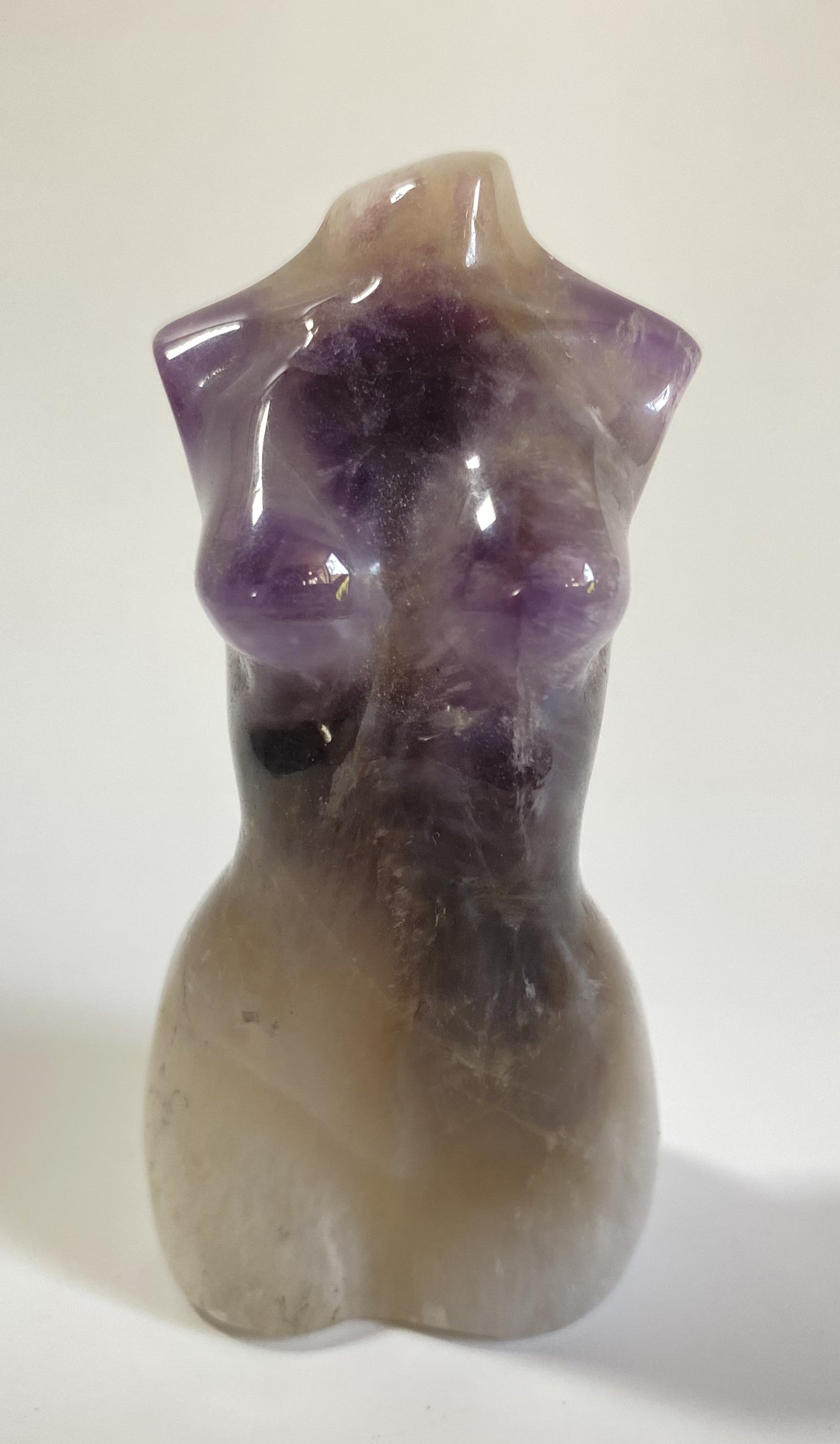 Sculptura in forma de nud din cristal de ametist chevron pe fundal alb sub lumina naturala