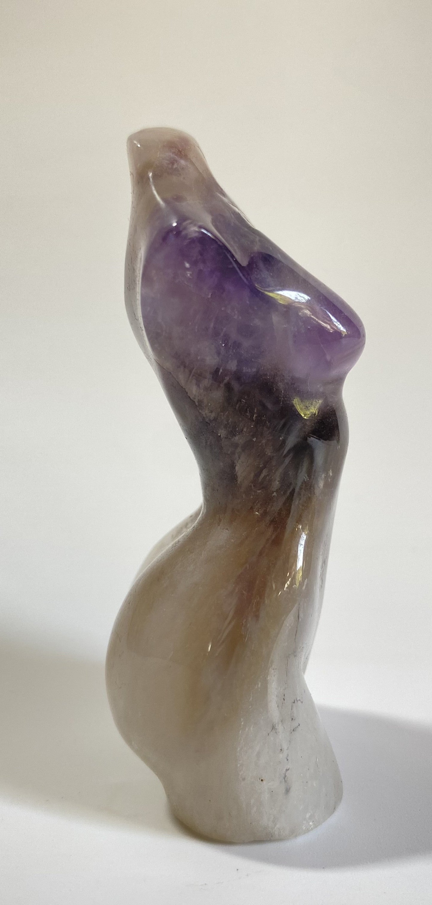 Sculptura in forma de nud din cristal de ametist chevron pe fundal alb sub lumina naturala