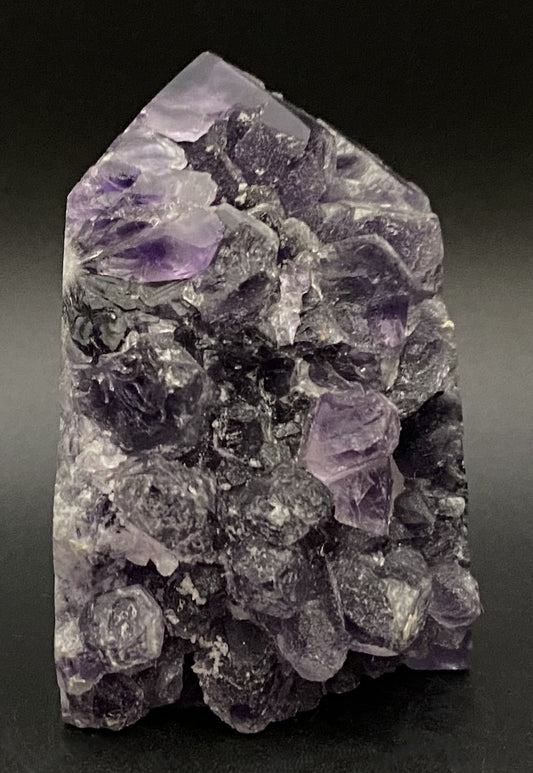 Obelisc din geoda de ametist pe fundal negru sub lumina artificiala