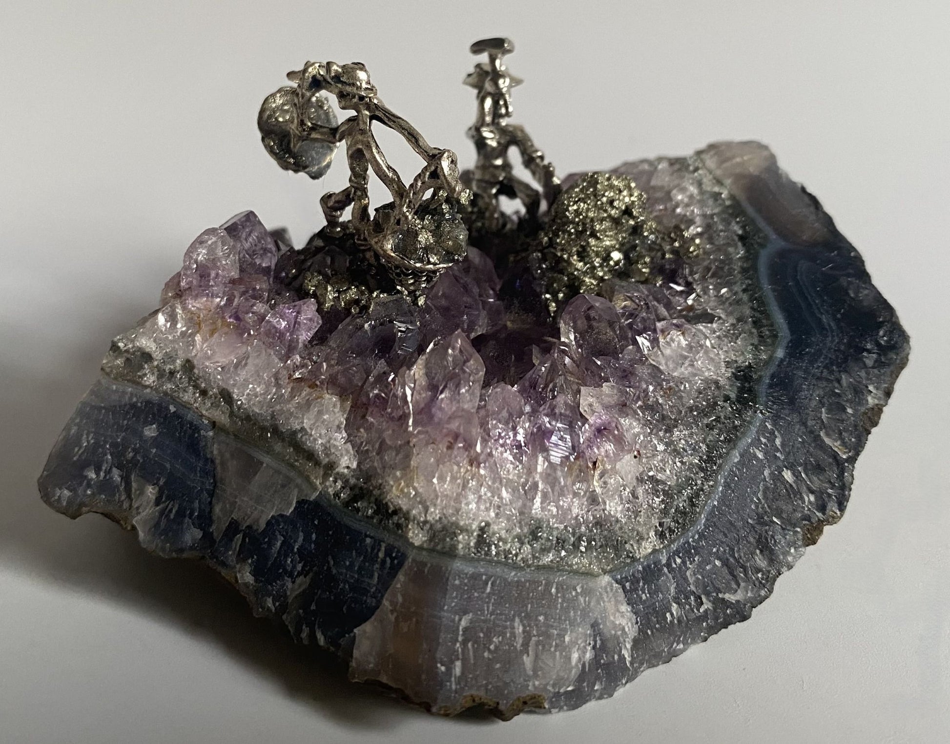 Geoda din piatra semipretioasa de ametist cu miniaturi de mineri metalice pe fundal alb