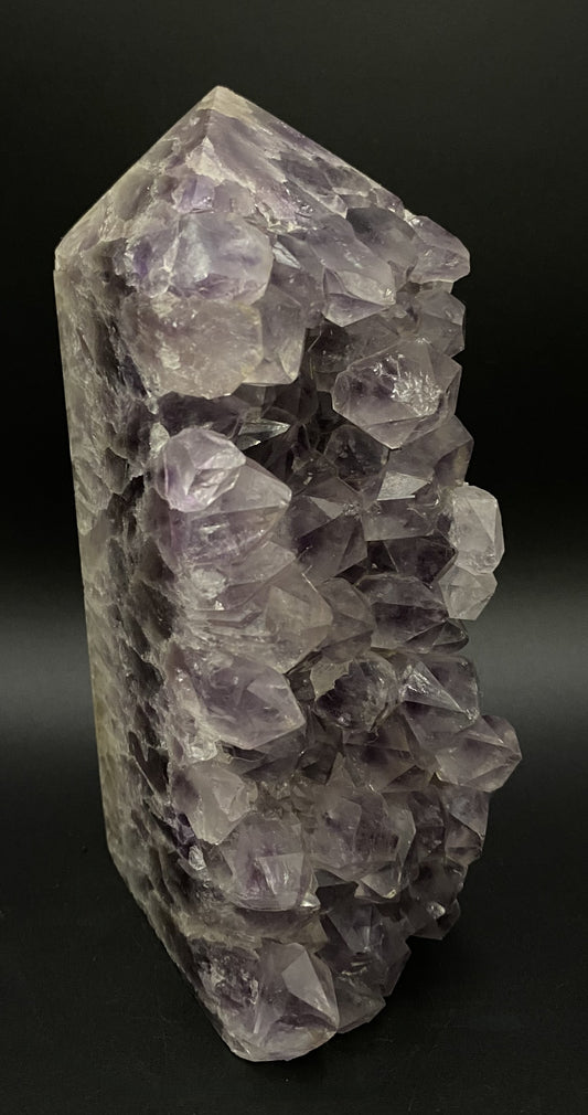 Obelisc din geoda de ametist pe fundal negru sub lumina artificiala