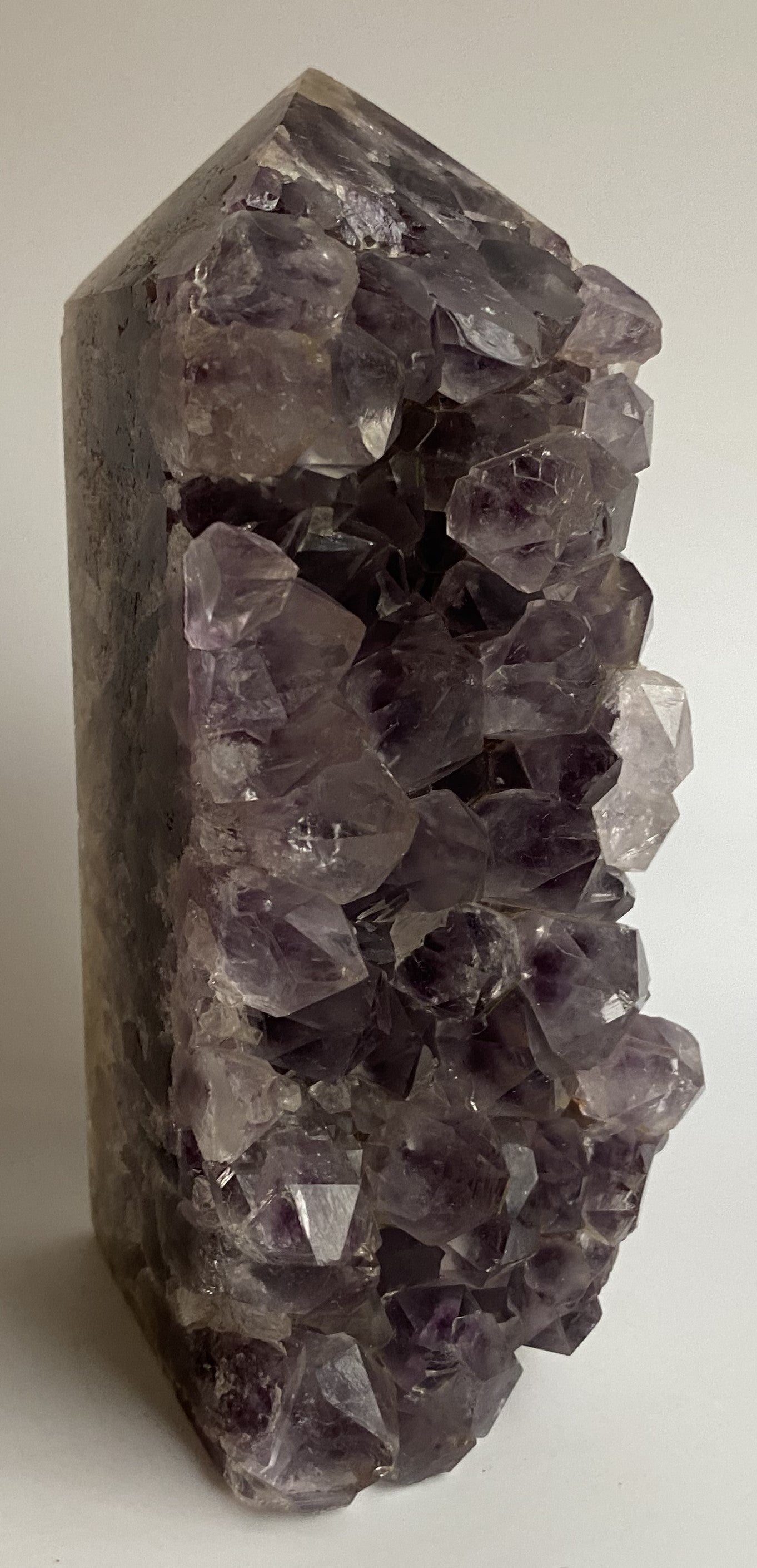 Obelisc din geoda de ametist pe fundal alb sub lumina naturala