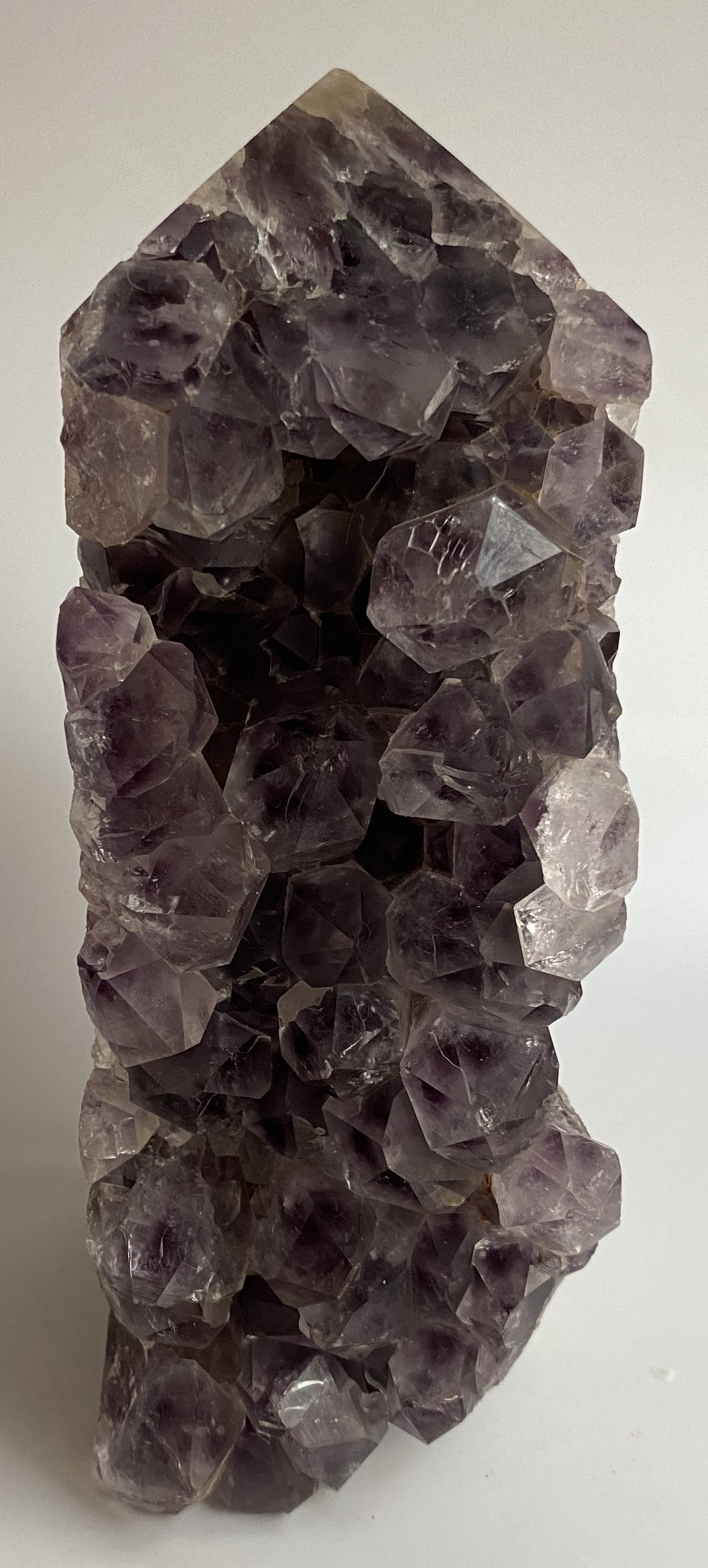 Obelisc din geoda de ametist pe fundal alb sub lumina naturala