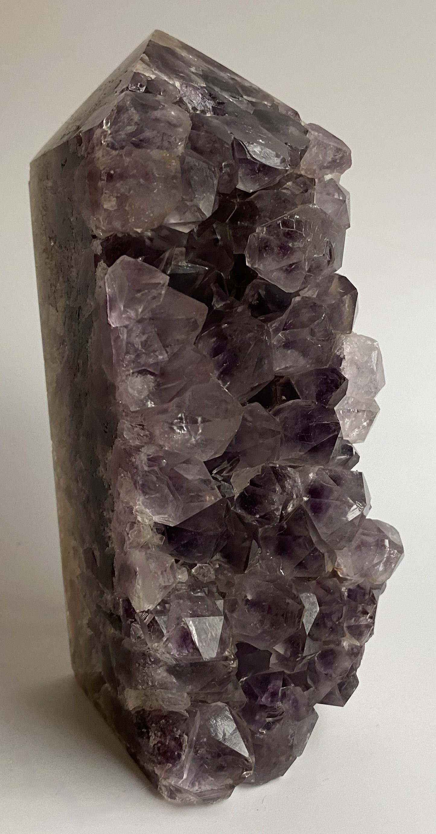 Obelisc din geoda de ametist pe fundal alb sub lumina naturala