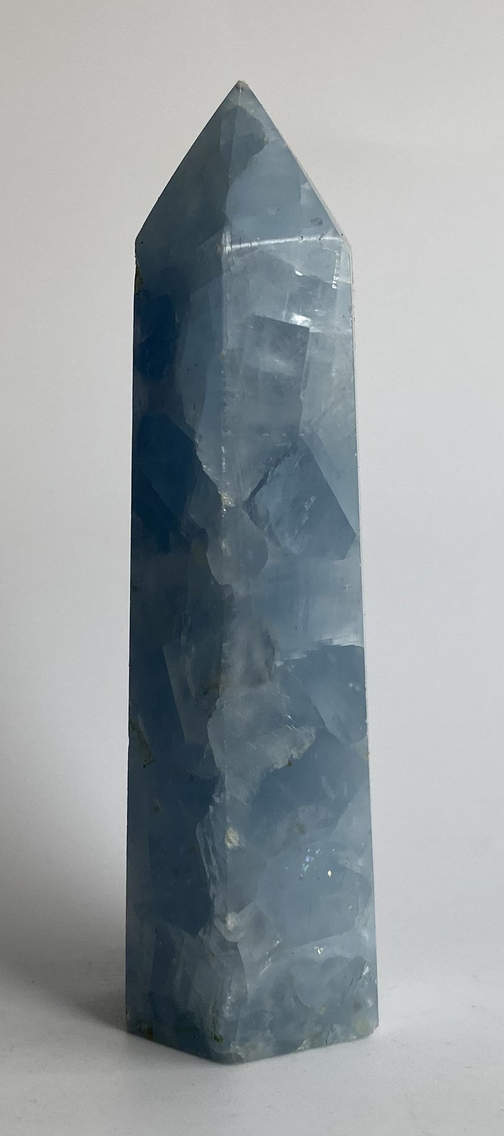 Obelisc din cristal de calcit albastru pe fundal alb sub lumina naturala