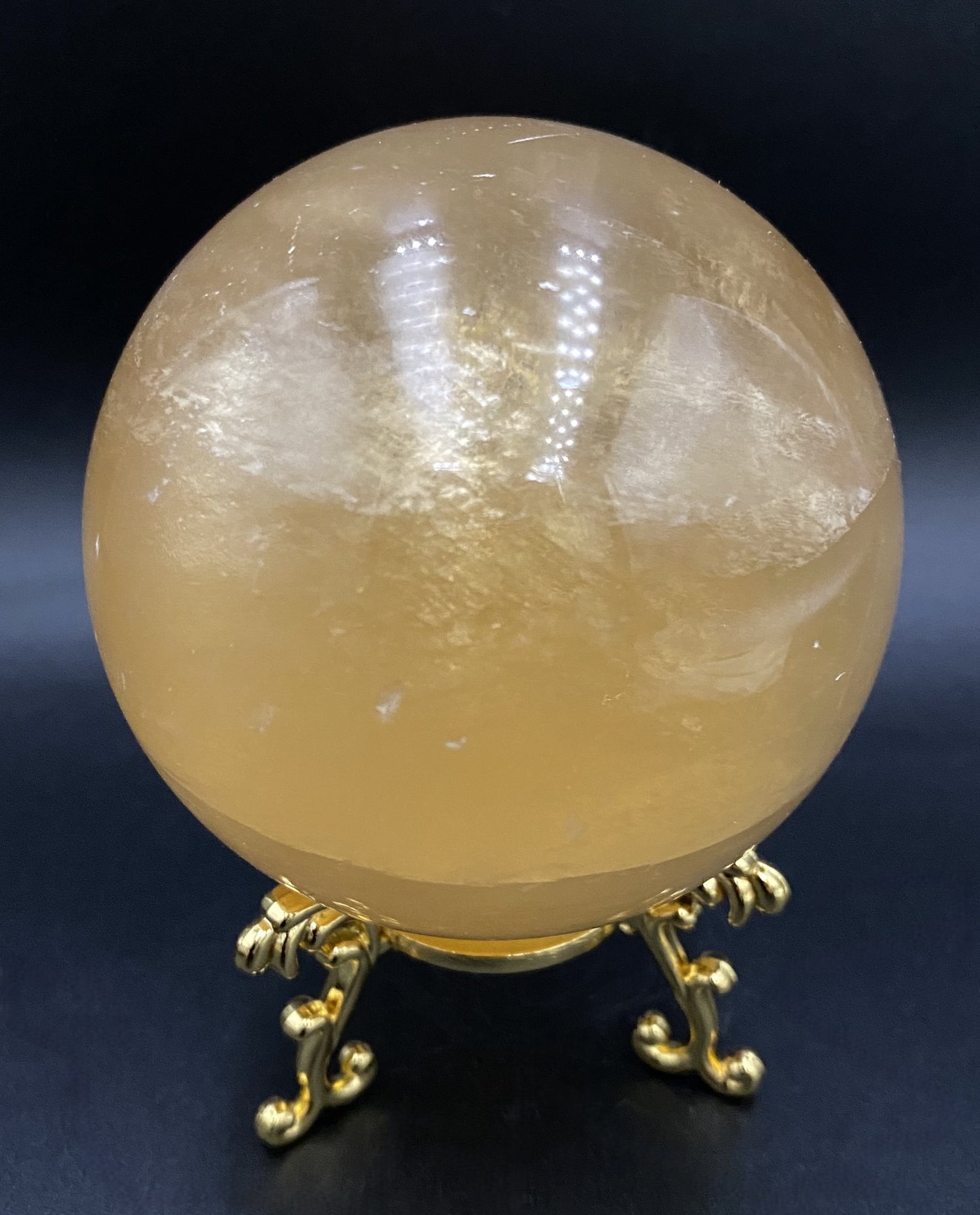Sfera din cristal de calcit galben pe suport metalic auriu, cu fundal negru sub lumina artificiala