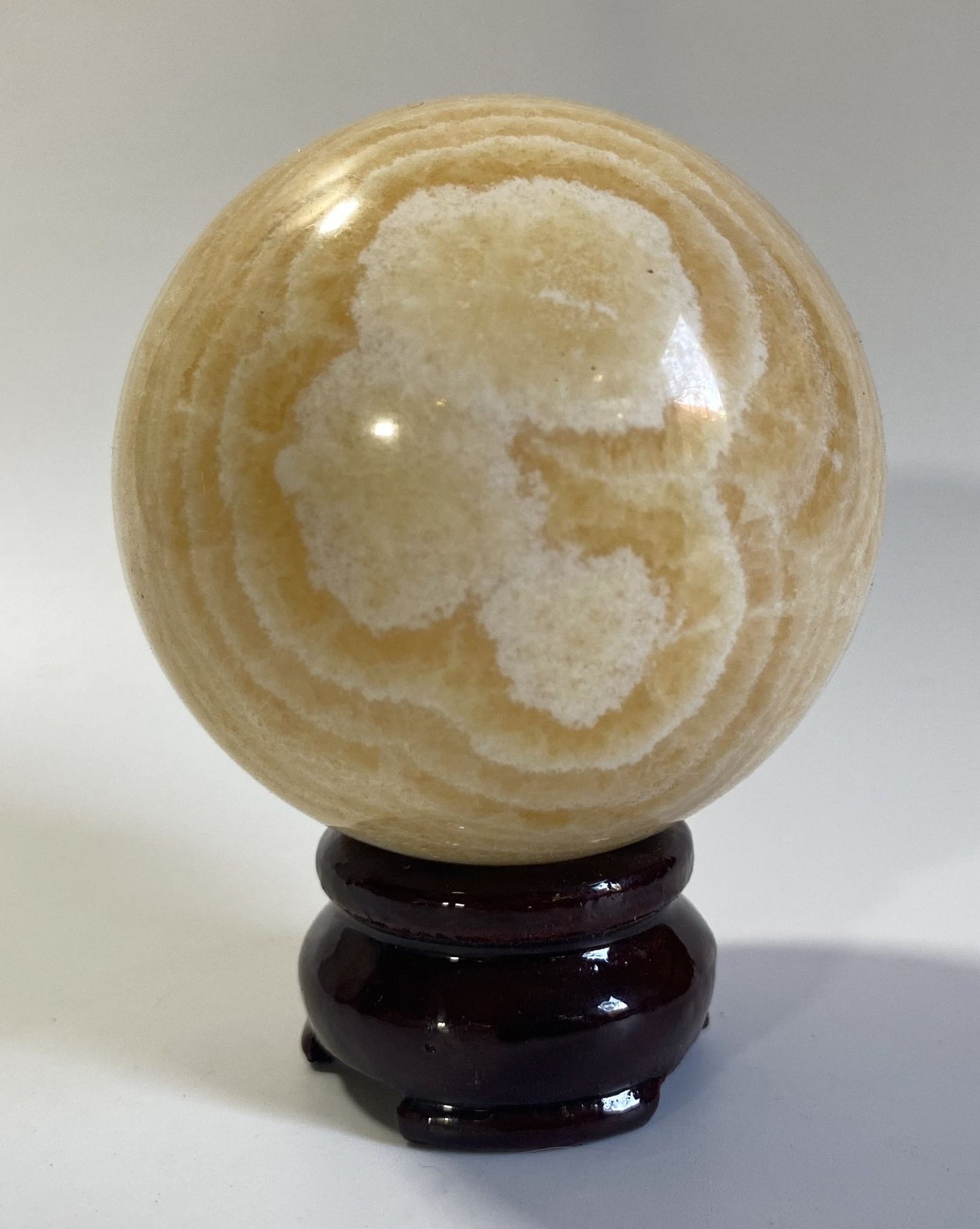 Sfera din cristal de calcit galben pe suport din lemn cu fundal alb