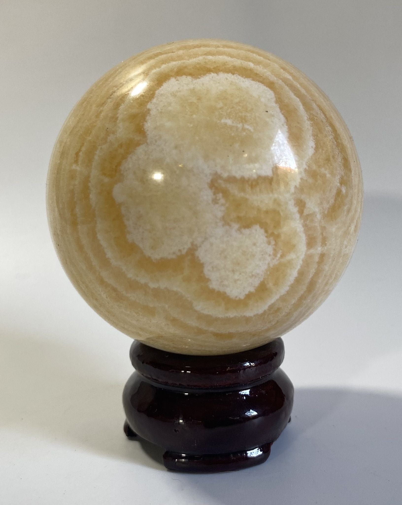 Sfera din cristal de calcit galben pe suport din lemn cu fundal alb