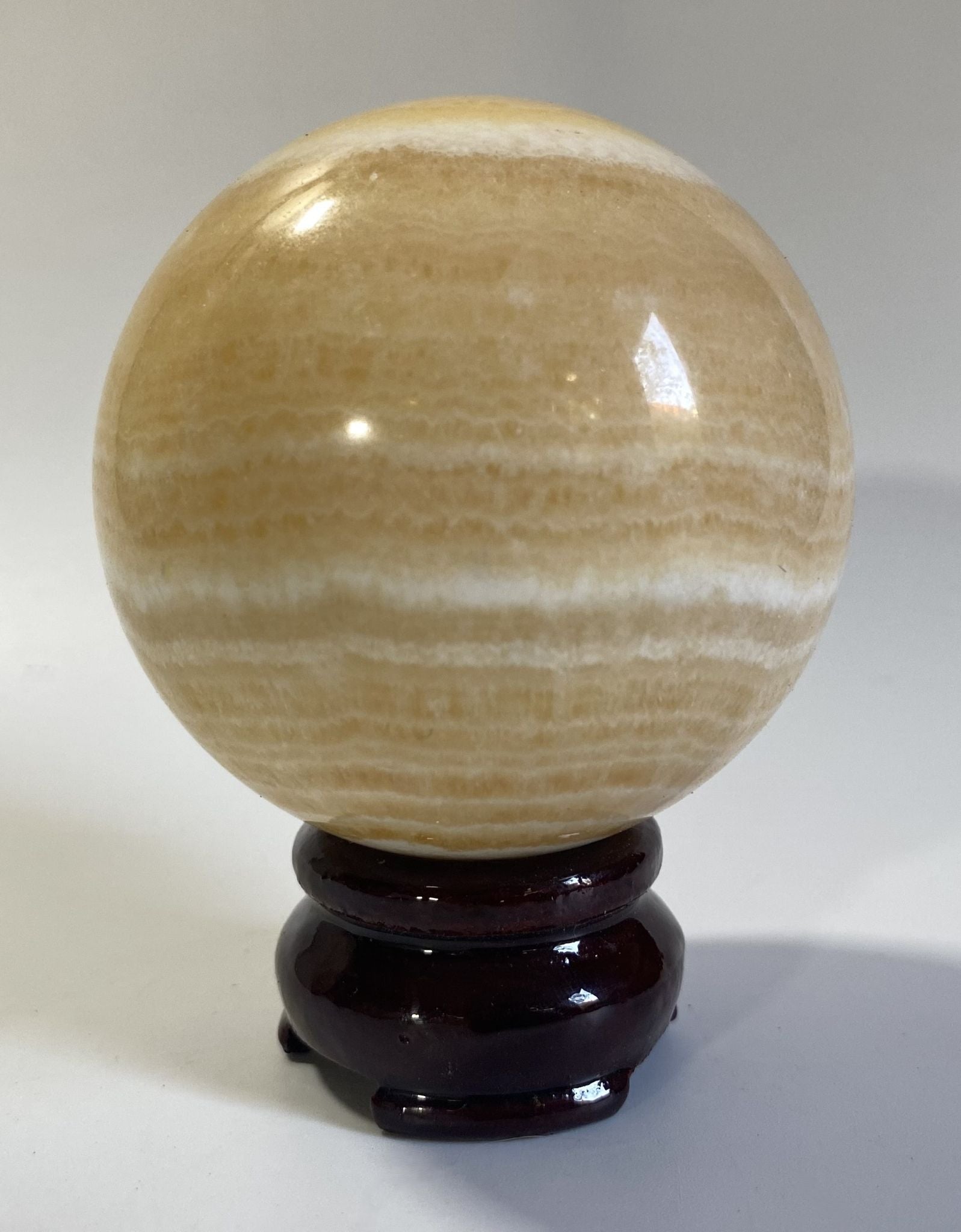 Sfera de 7.1cm din piatra semipretioasa de calcit galben pe suport din lemn cu fundal alb