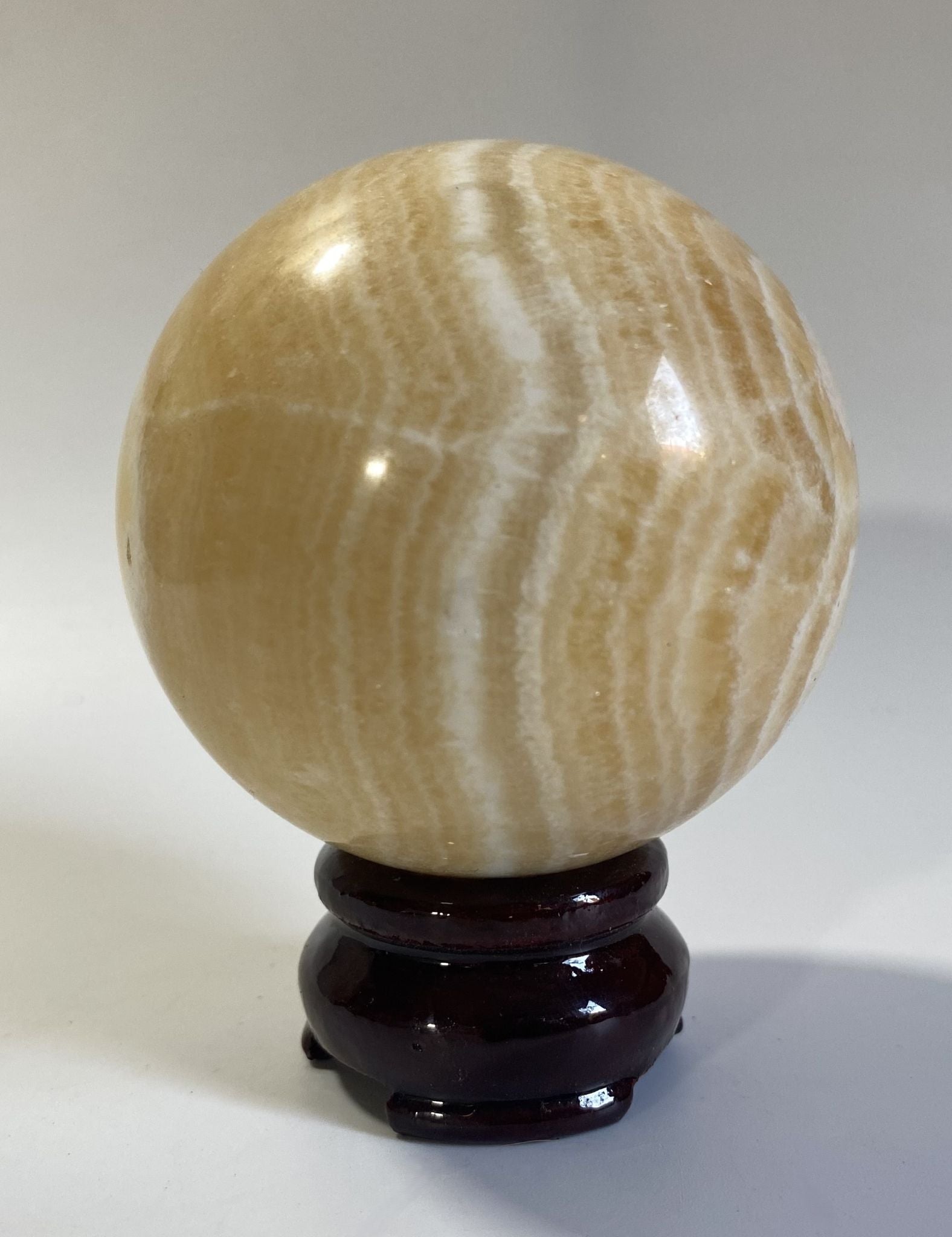 Sfera decorativa de 7.1cm din piatra semipretioasa de calcit galben pe suport din lemn cu fundal alb