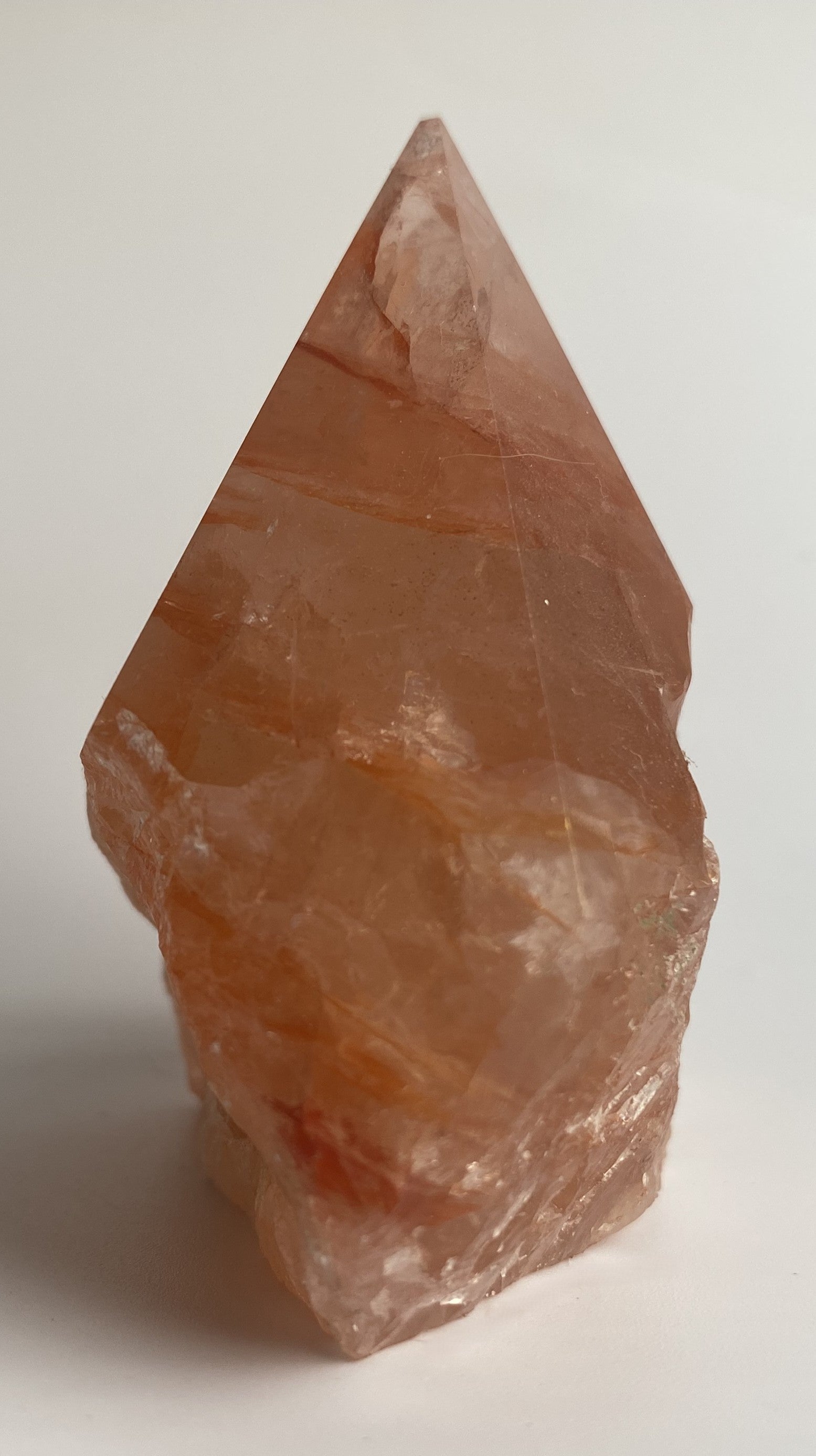 Varf polisat din cristal de cuart hematoid rosu pe fundal alb sub lumina naturala