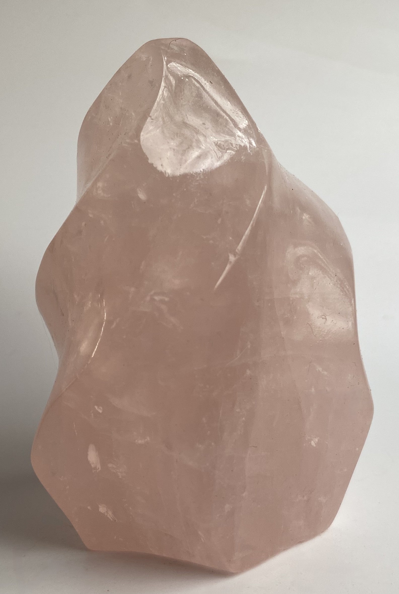 Sculptura din cristal de cuart roz pe fundal alb sub lumina naturala