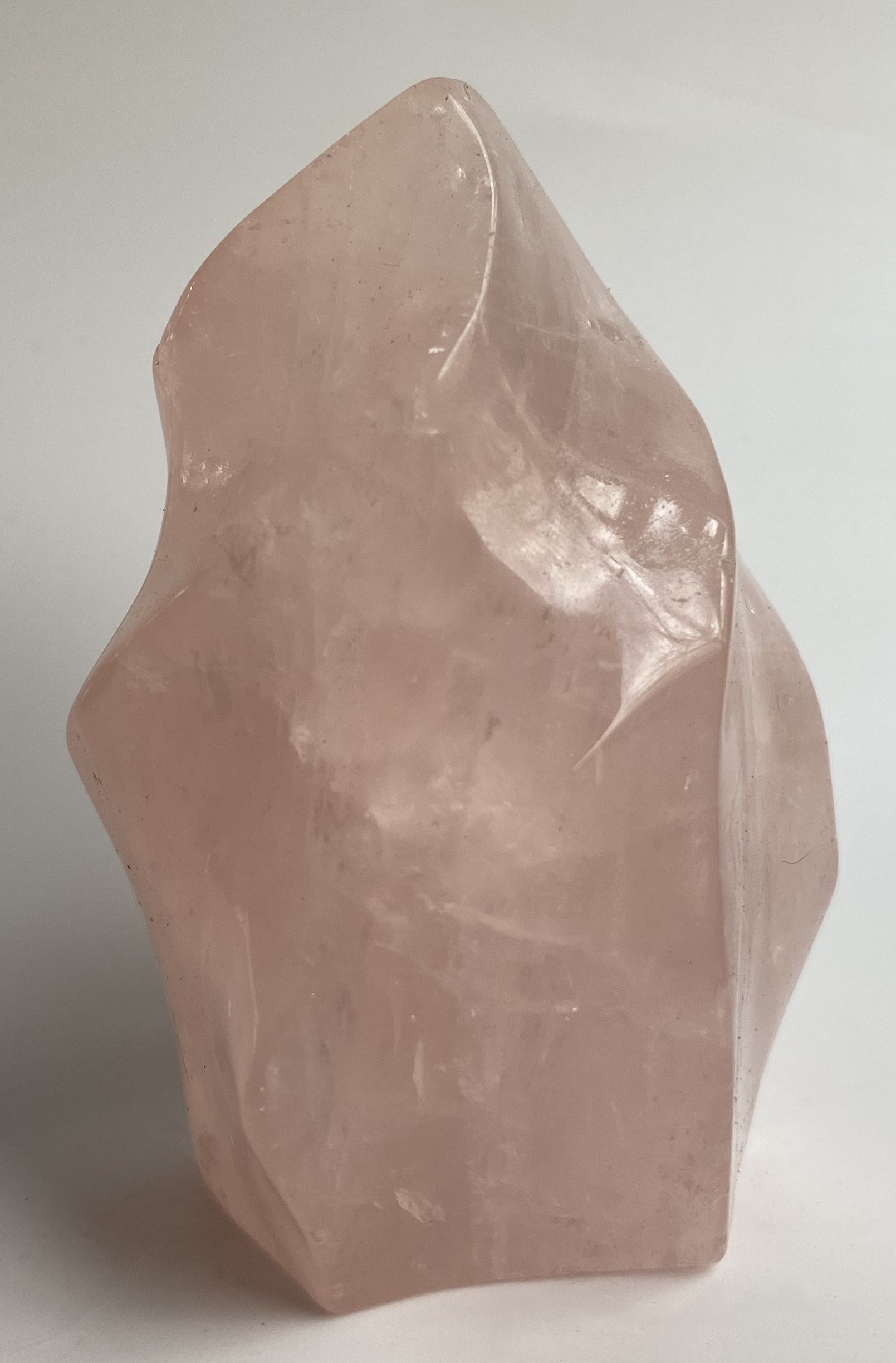Sculptura din cristal de cuart roz pe fundal alb sub lumina naturala