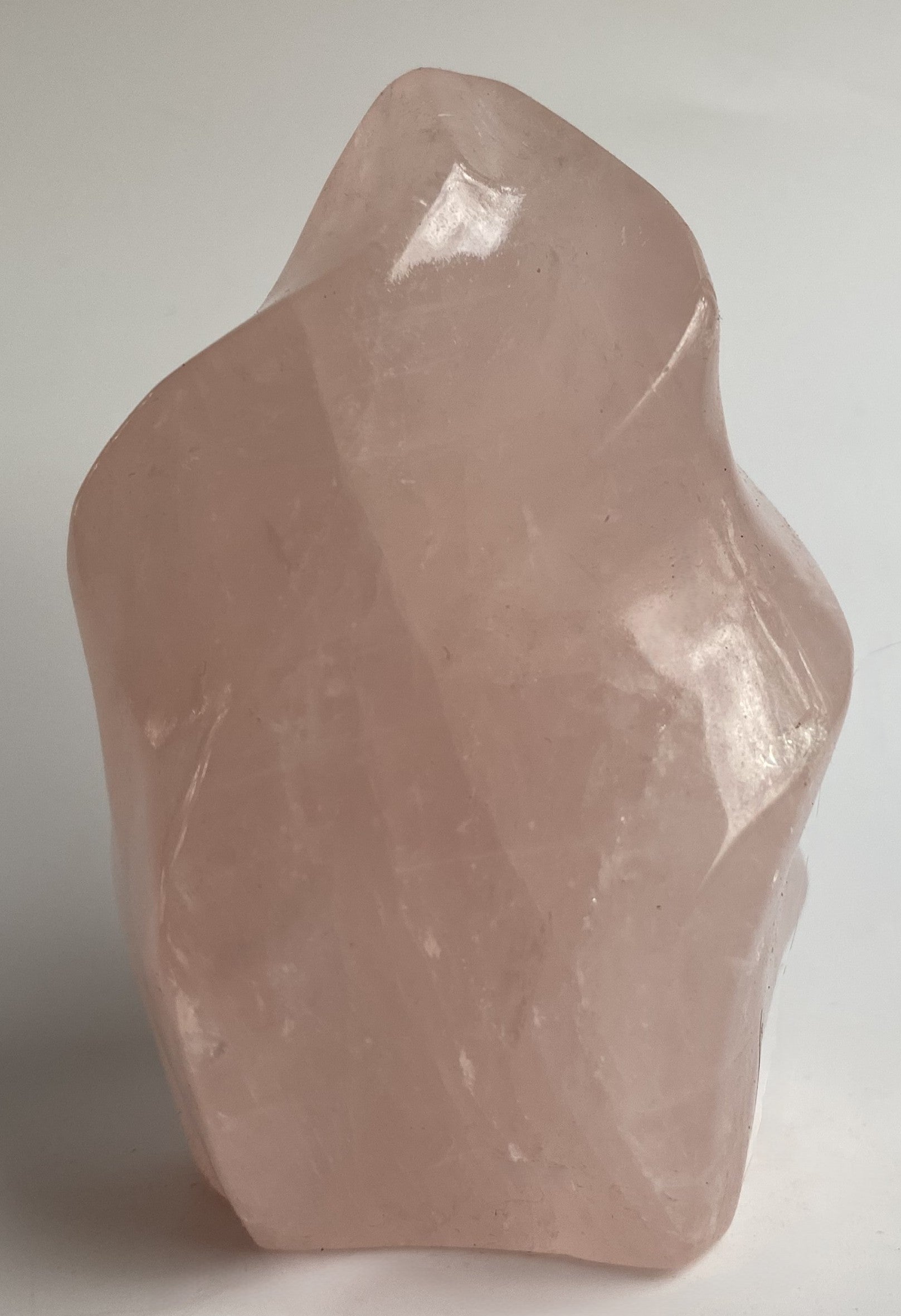 Sculptura din cristal de cuart roz pe fundal alb sub lumina naturala