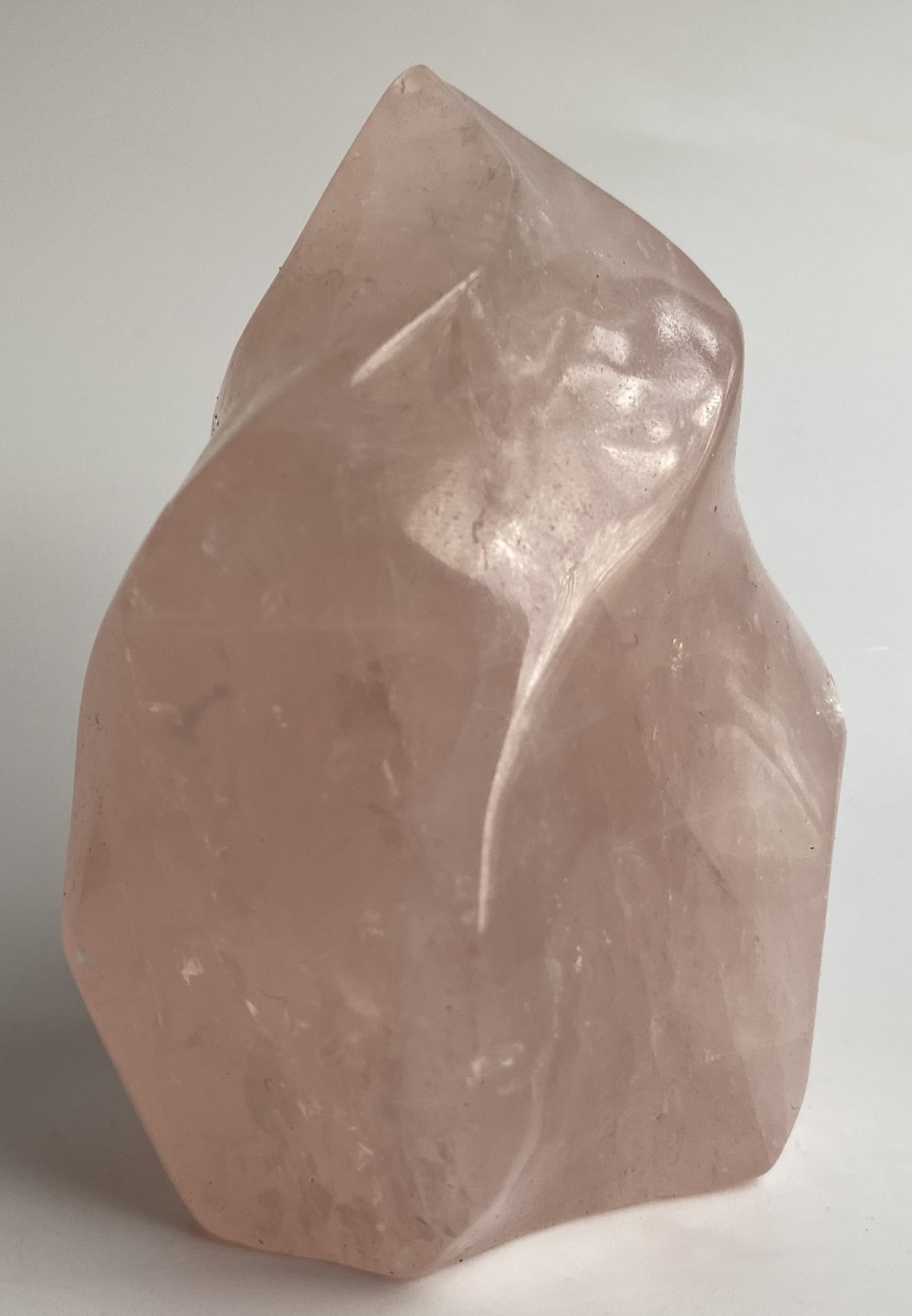 Sculptura din cristal de cuart roz pe fundal alb sub lumina naturala