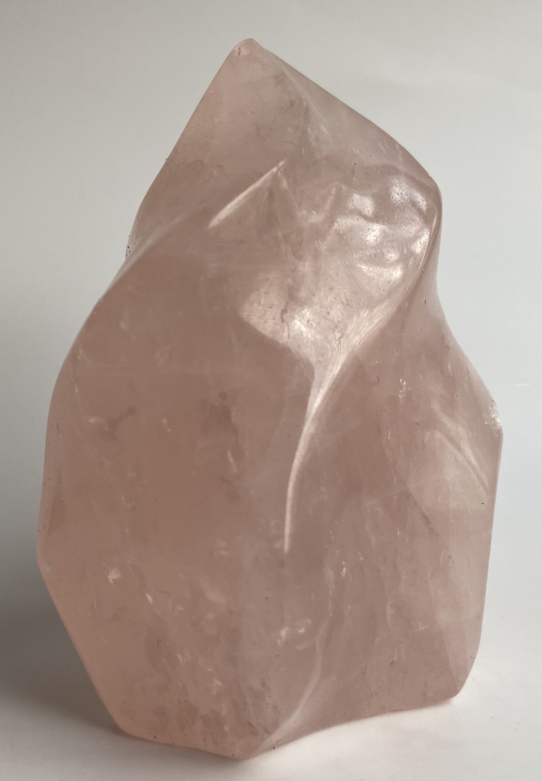 Sculptura din cristal de cuart roz pe fundal alb sub lumina naturala