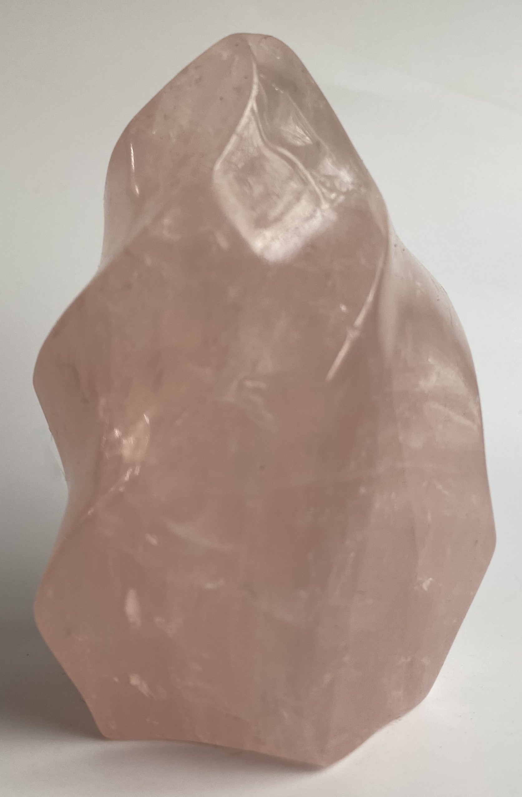 Sculptura din cristal de cuart roz pe fundal alb sub lumina naturala