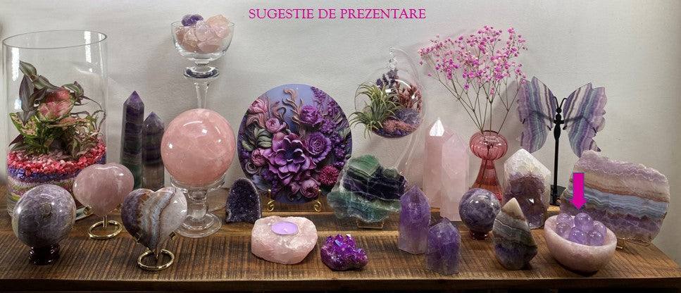 Rose quartz bowl among various decorative and healing crystals on wooden surface