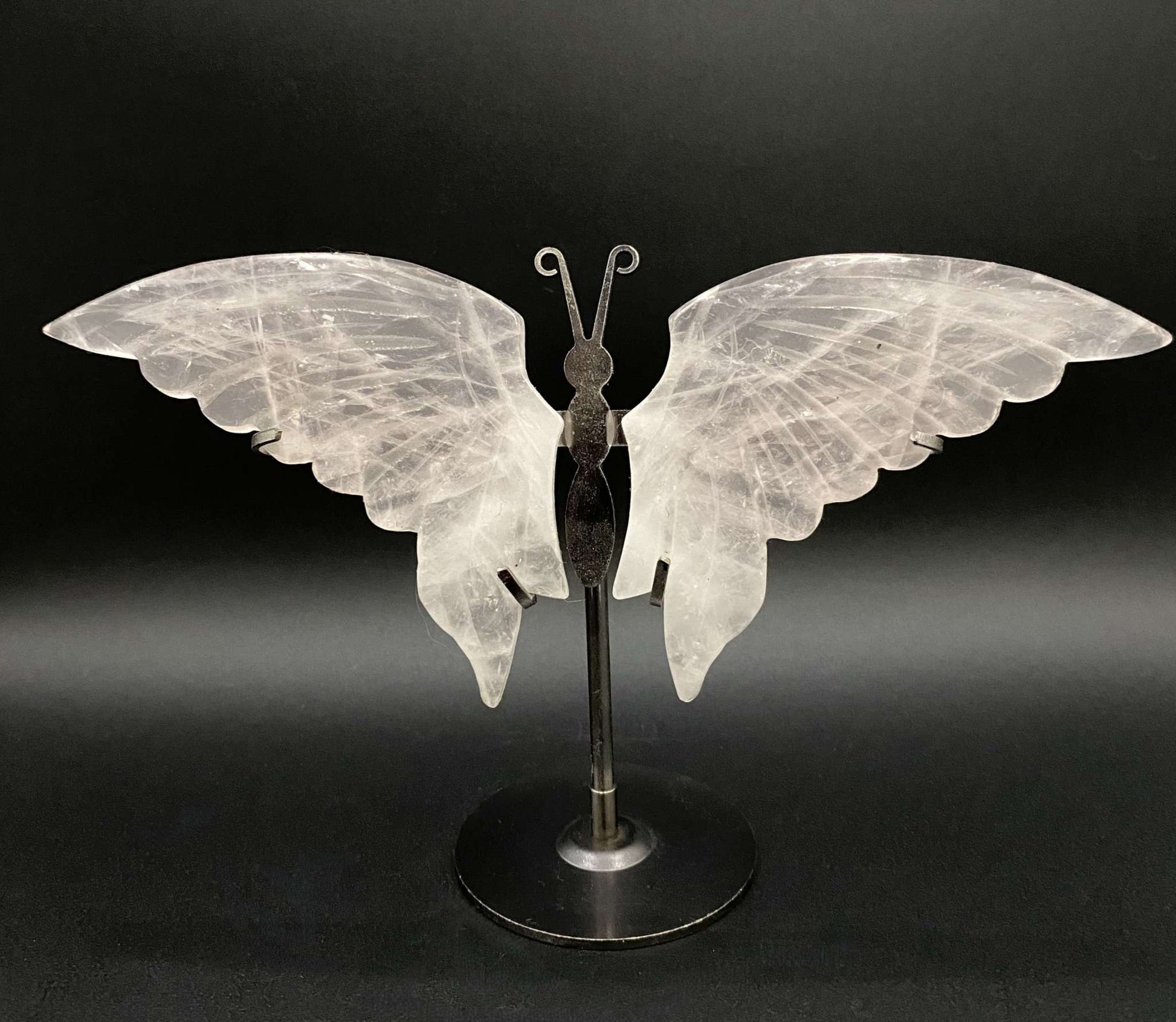 Butterfly sculpture made of rose quartz on a metal stand against a black background