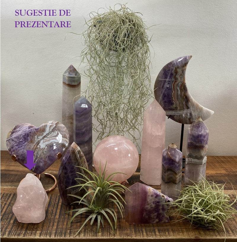 Sculptura din Cuart Roz piatra semipretioasa expusa pe masa cu alte cristale si plante verzi