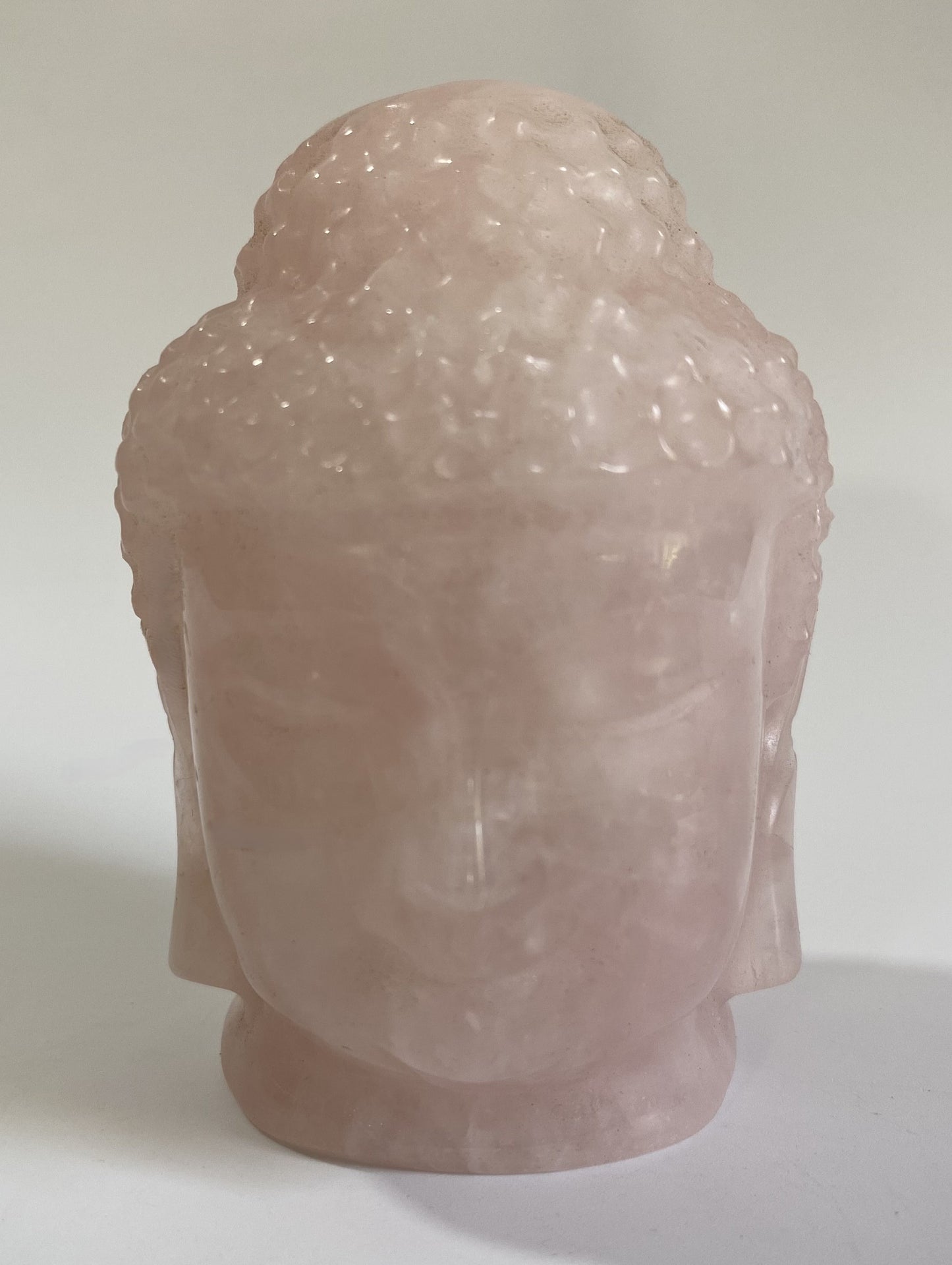 Sculptura Buddha din cuart roz pe fond alb sub lumina naturala